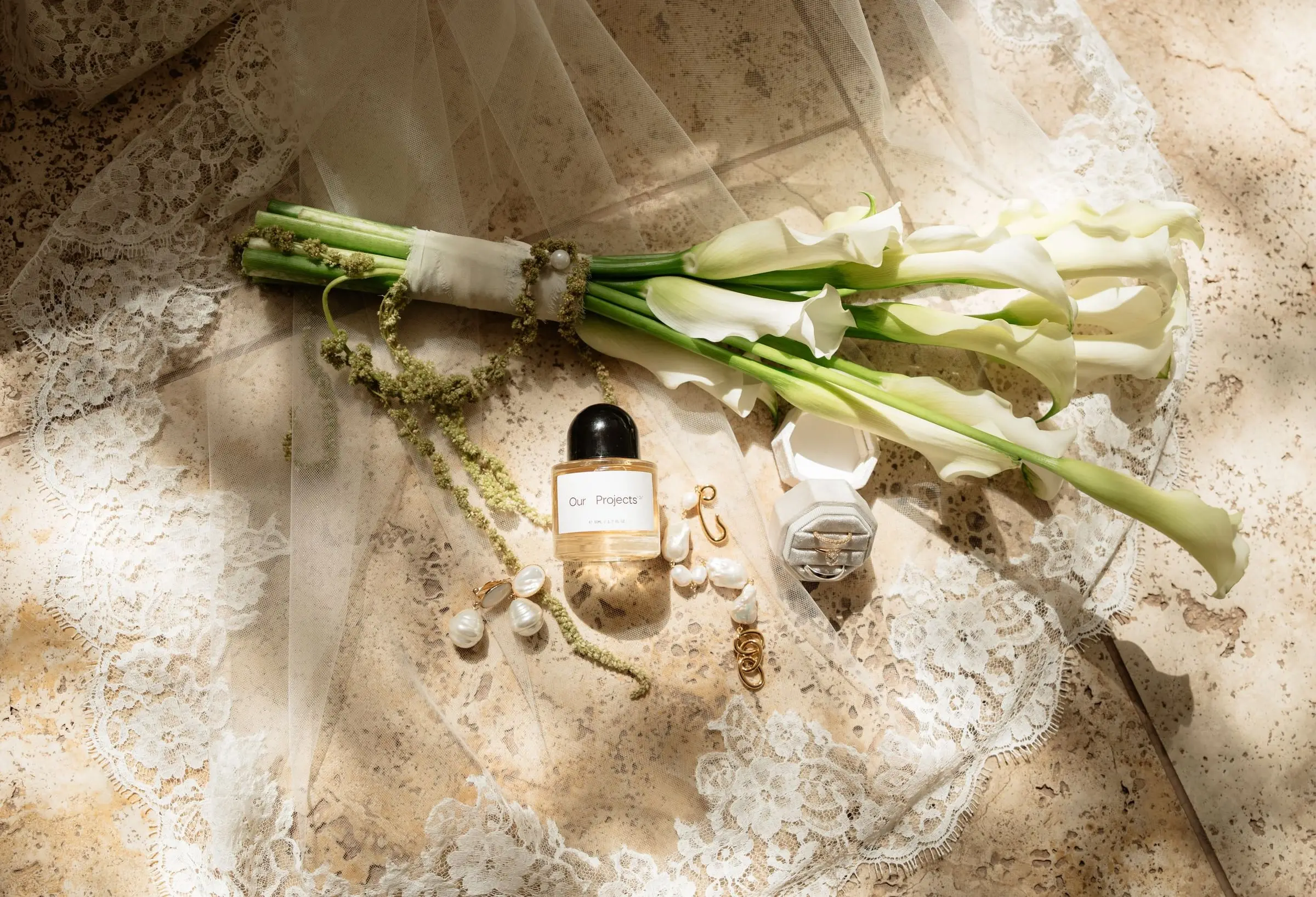 Calla lily bouquet, perfume and jewellery laid out on lace