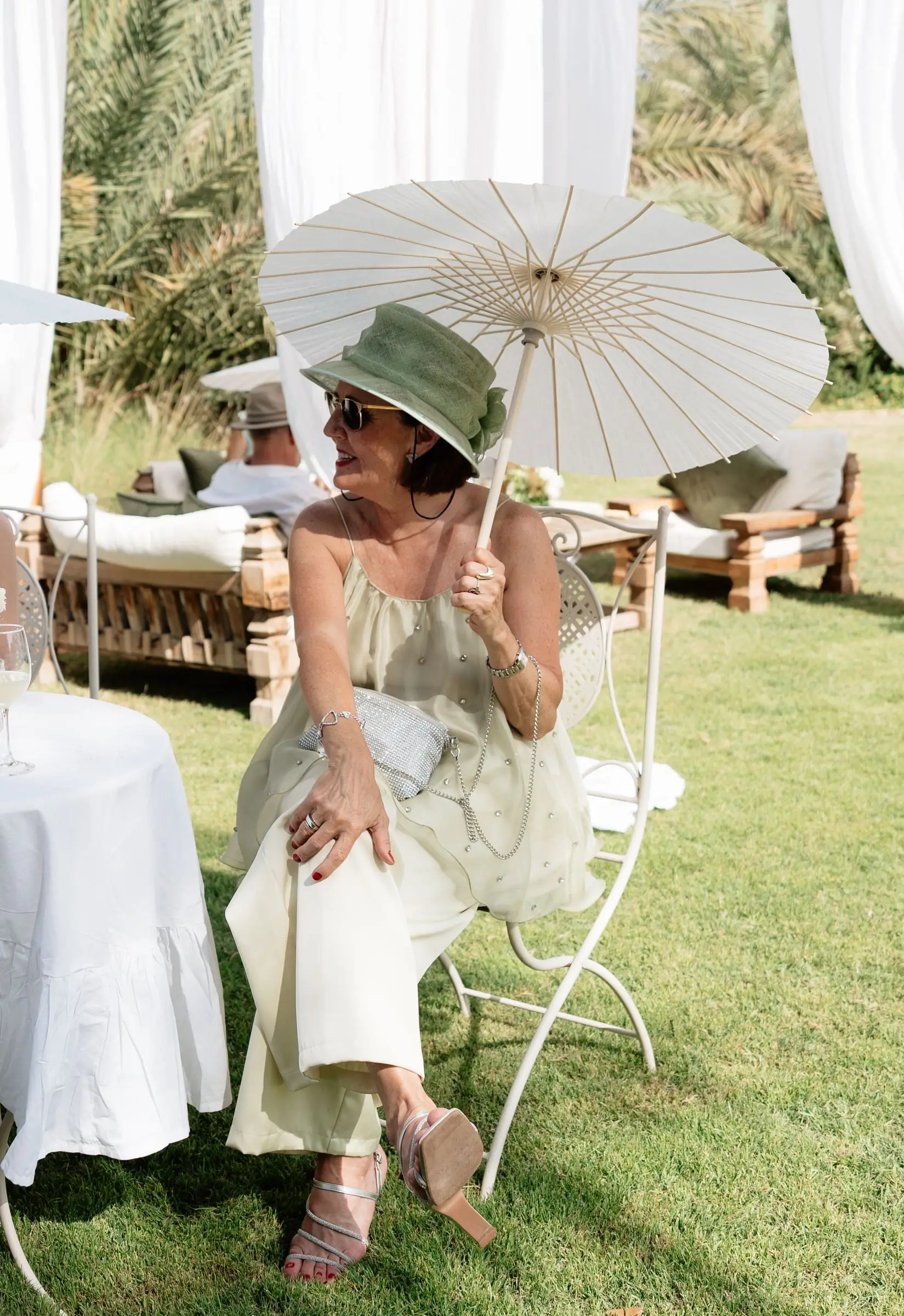 Guest in a green hat sitting under a white parasol in the garden