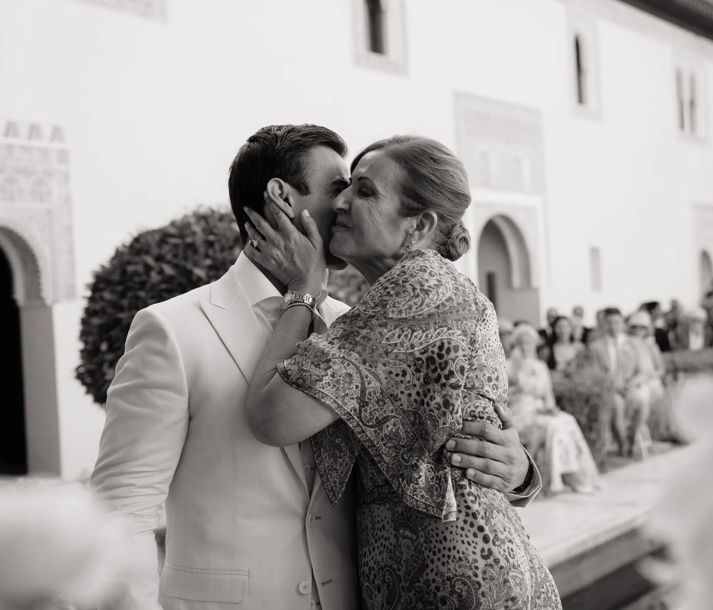 Black and white photo of the groom's mother kissing him before the ceremony