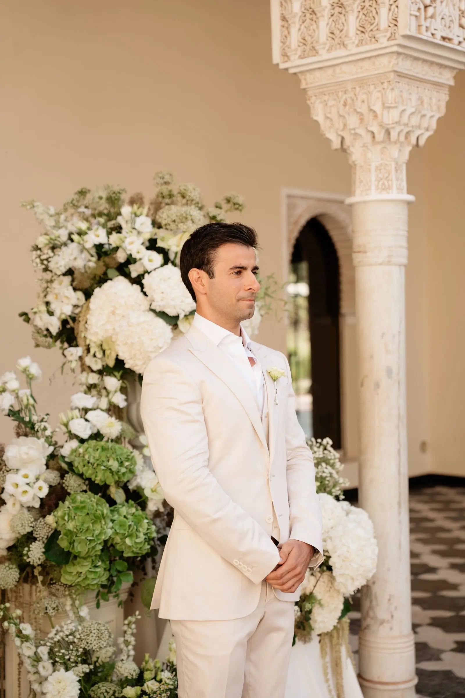 Groom in a cream suit waiting beside white hydrangeas
