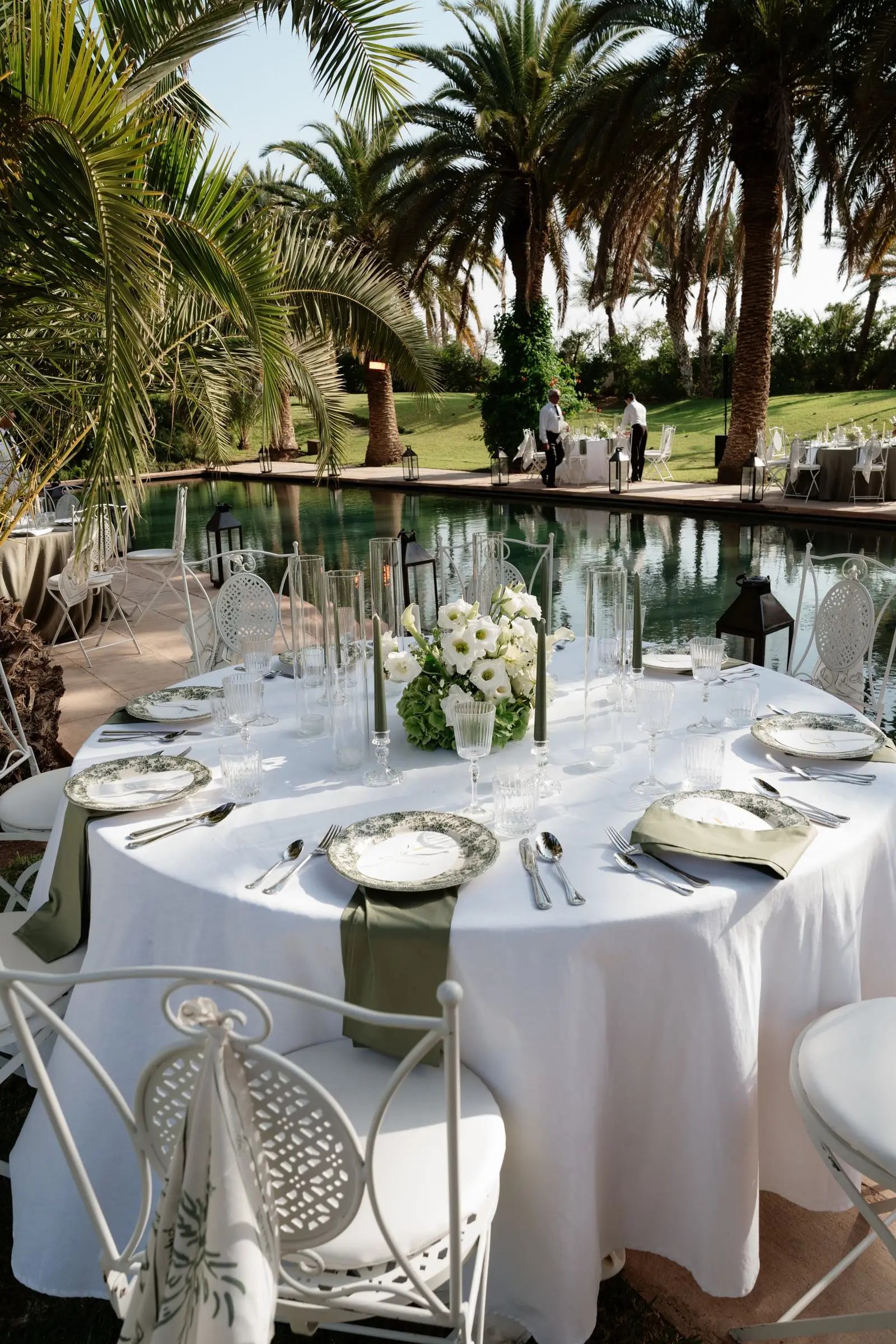 Round dinner table set beside the pool under palm trees