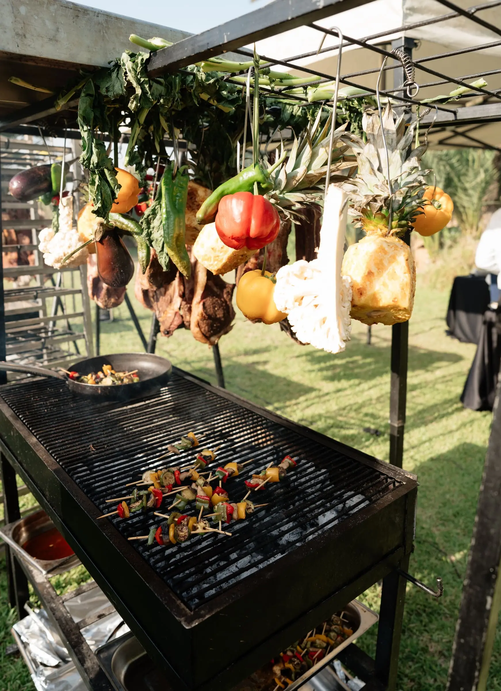 Barbecue station with hanging vegetables and skewers on the grill