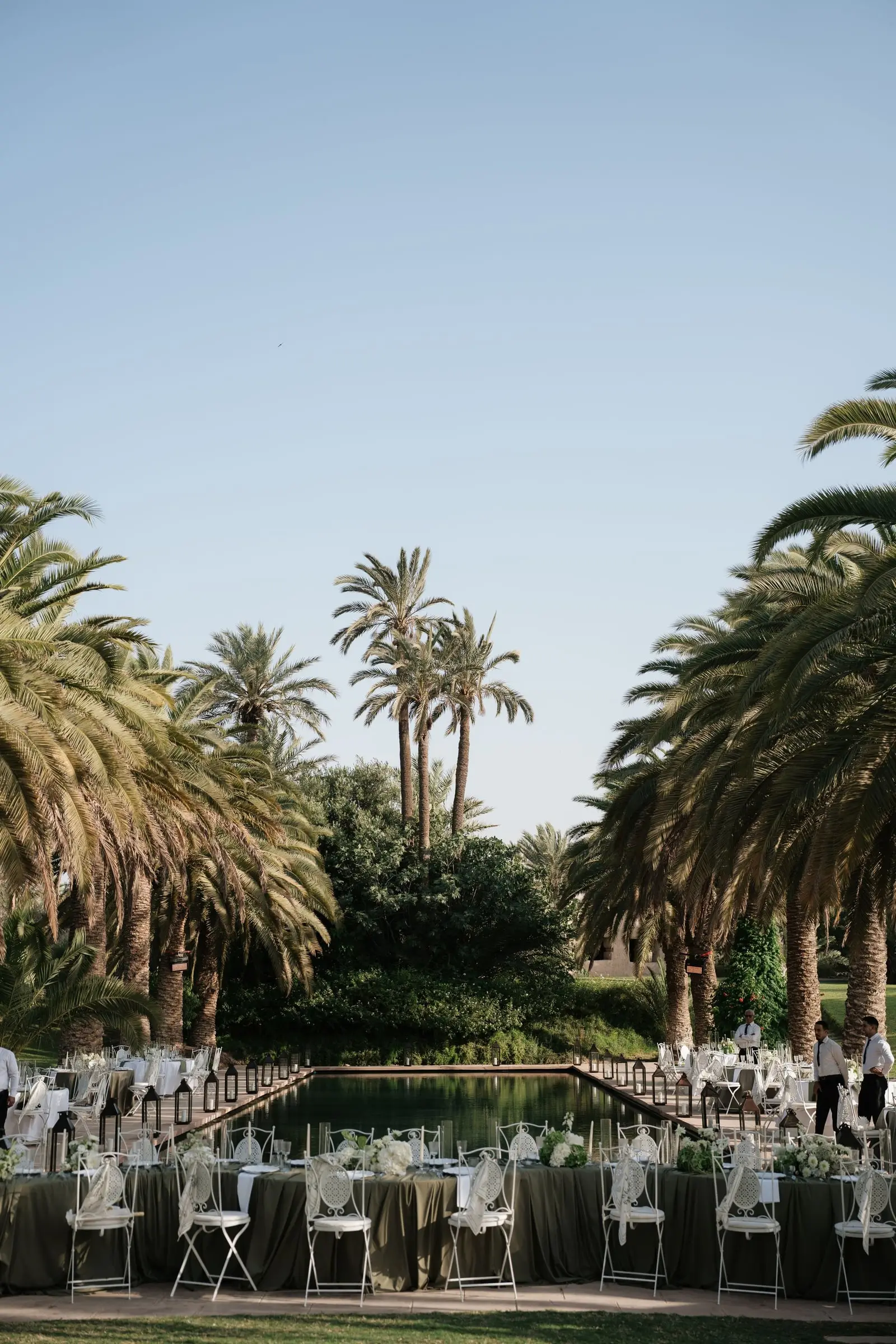 Tables set around the pool with palm trees against a clear sky