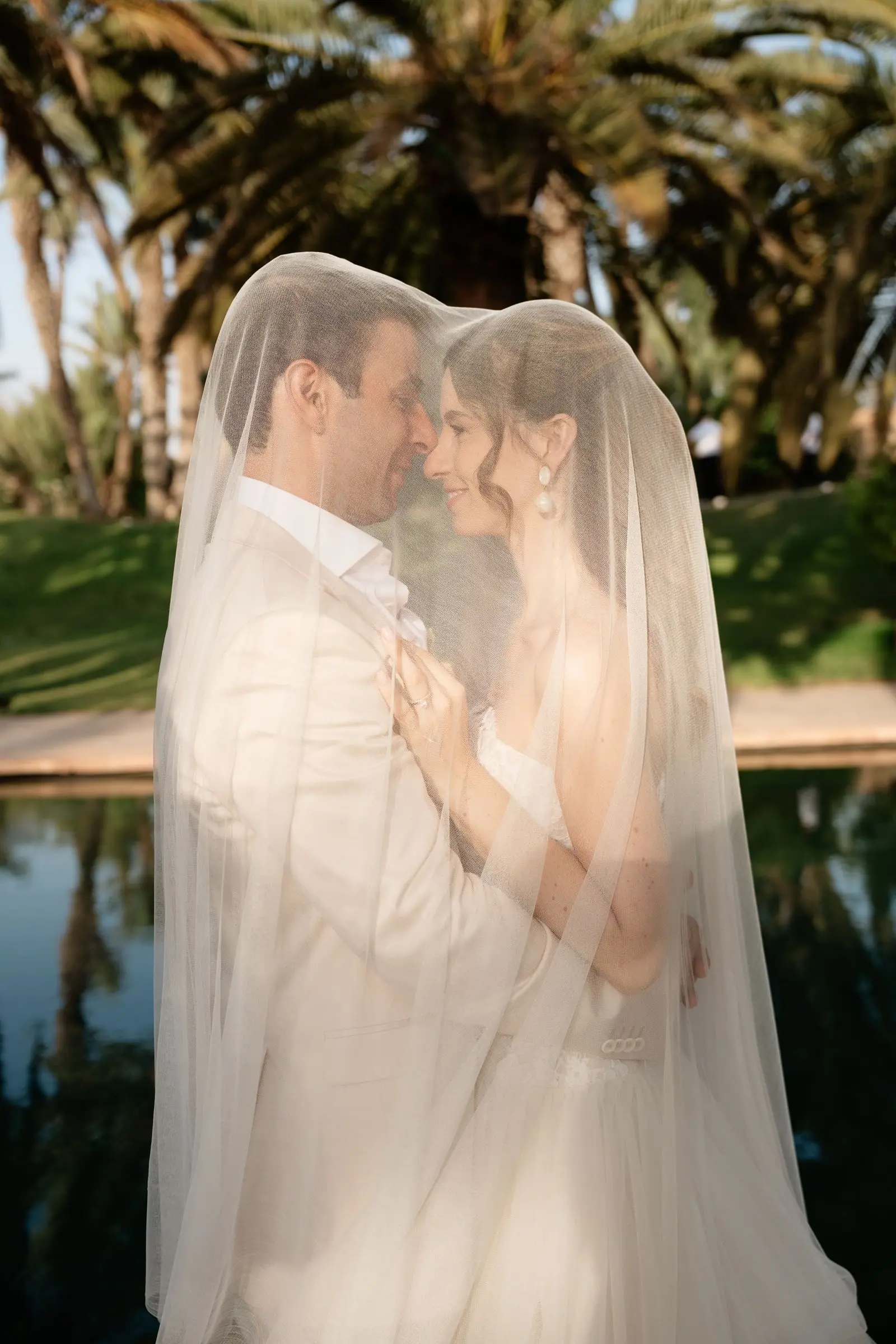 Couple embracing under the bride's long veil by the pool