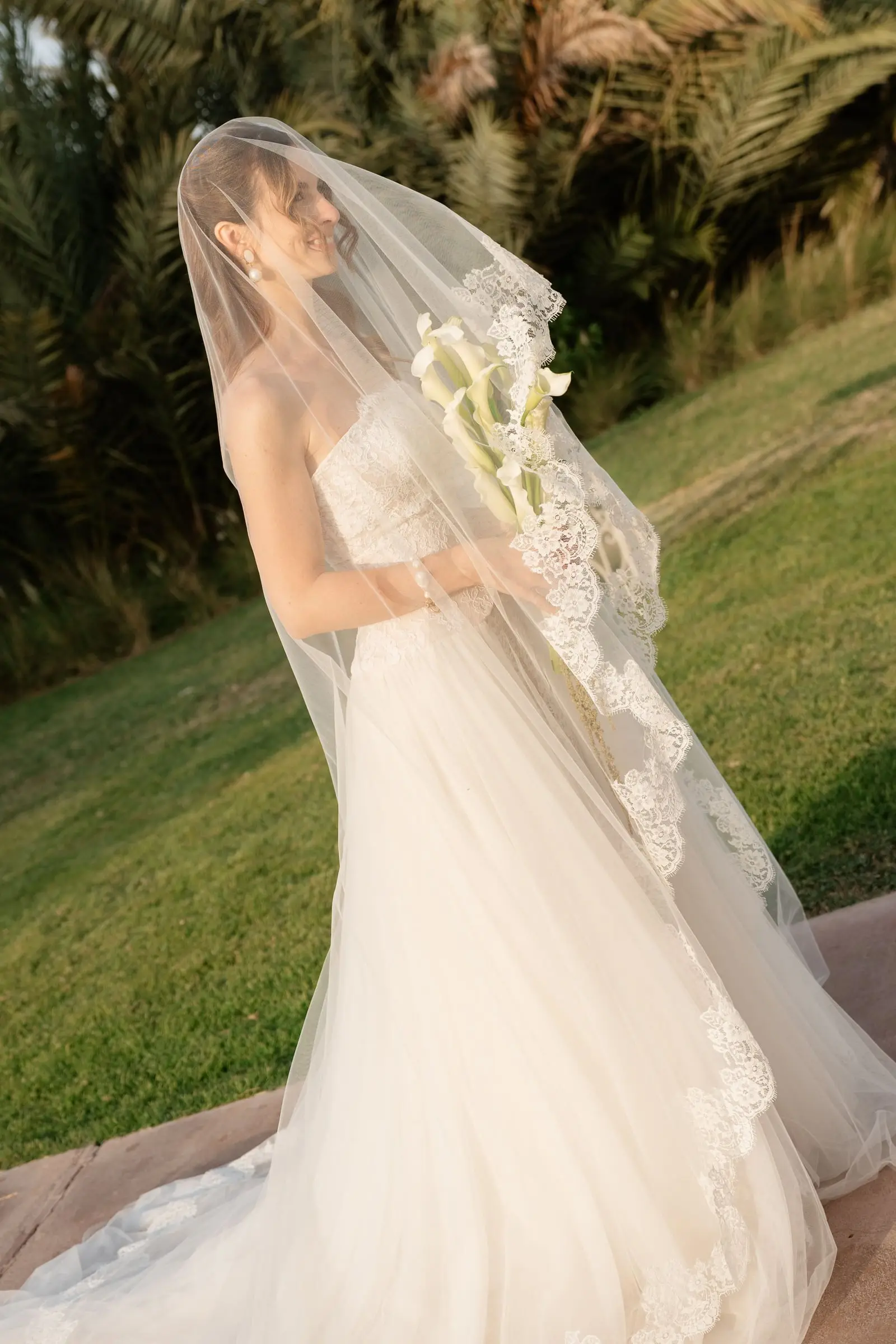Bride under her long veil holding calla lilies in the evening light