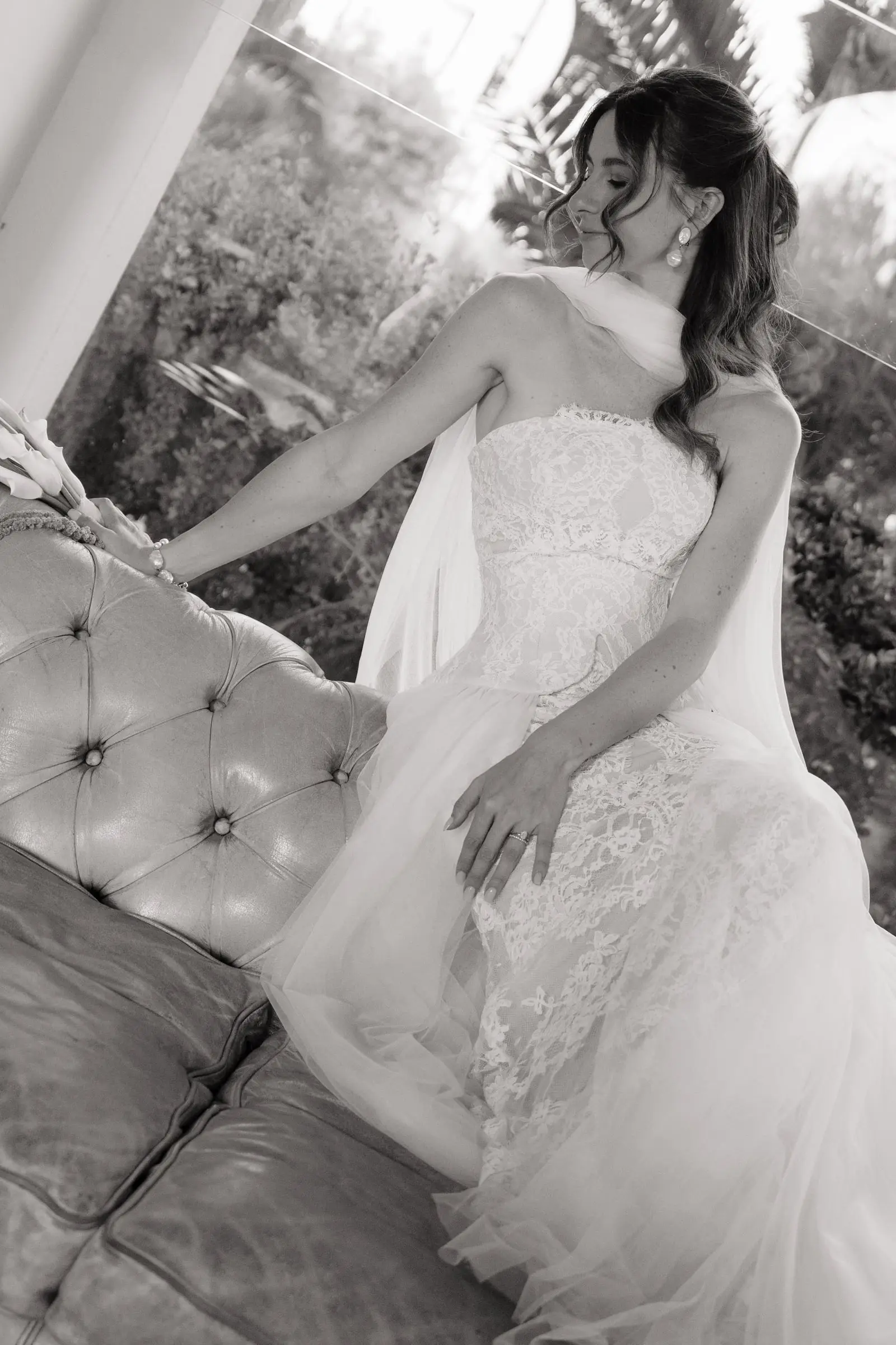 Black and white photo of the bride in her lace gown by a leather sofa