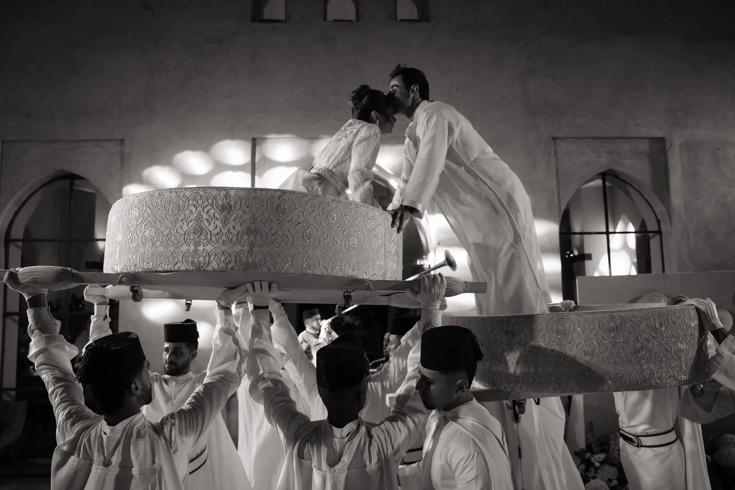 Black and white photo of the couple kissing on the raised Amaria thrones