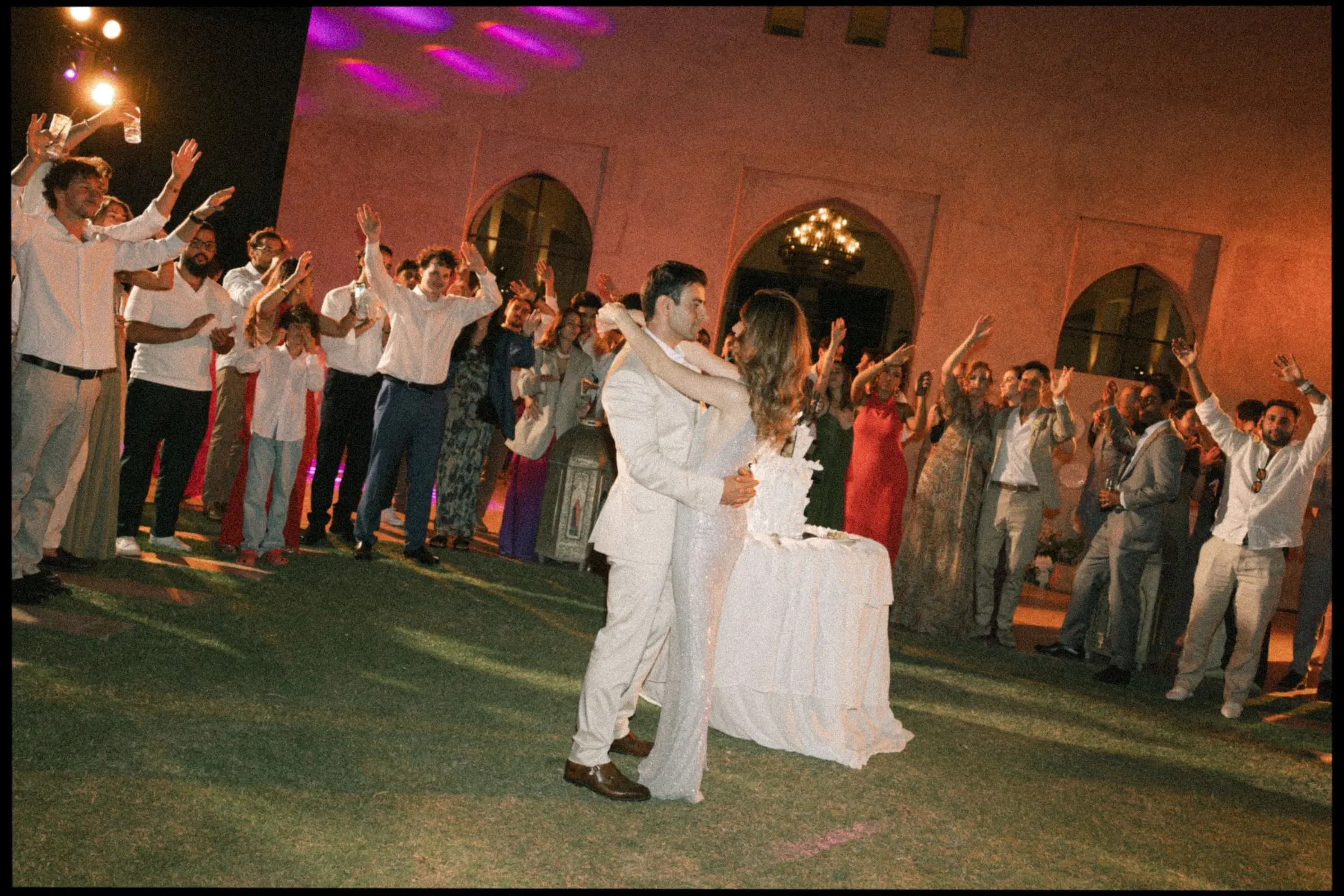 Couple dancing their first dance surrounded by guests at night, on film
