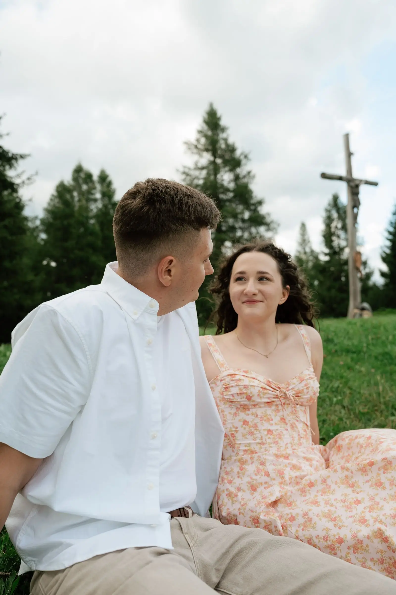 Couple sitting in the grass beside a wooden wayside cross above La Val