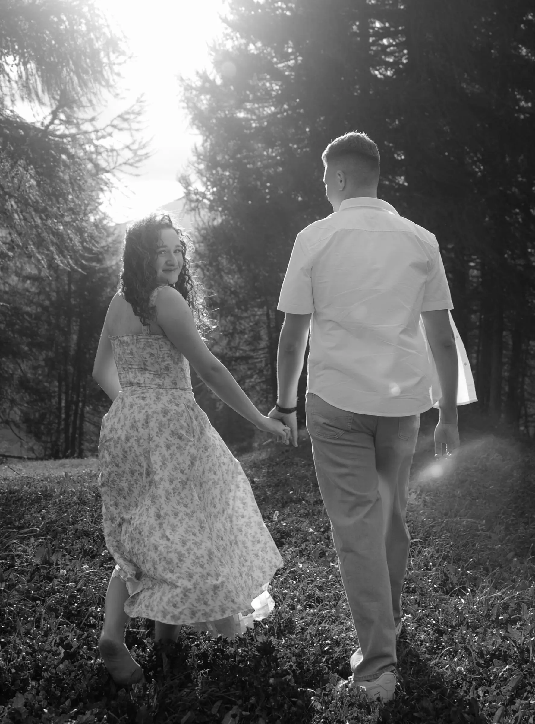 Black and white photo of the couple walking hand in hand through a sunlit forest