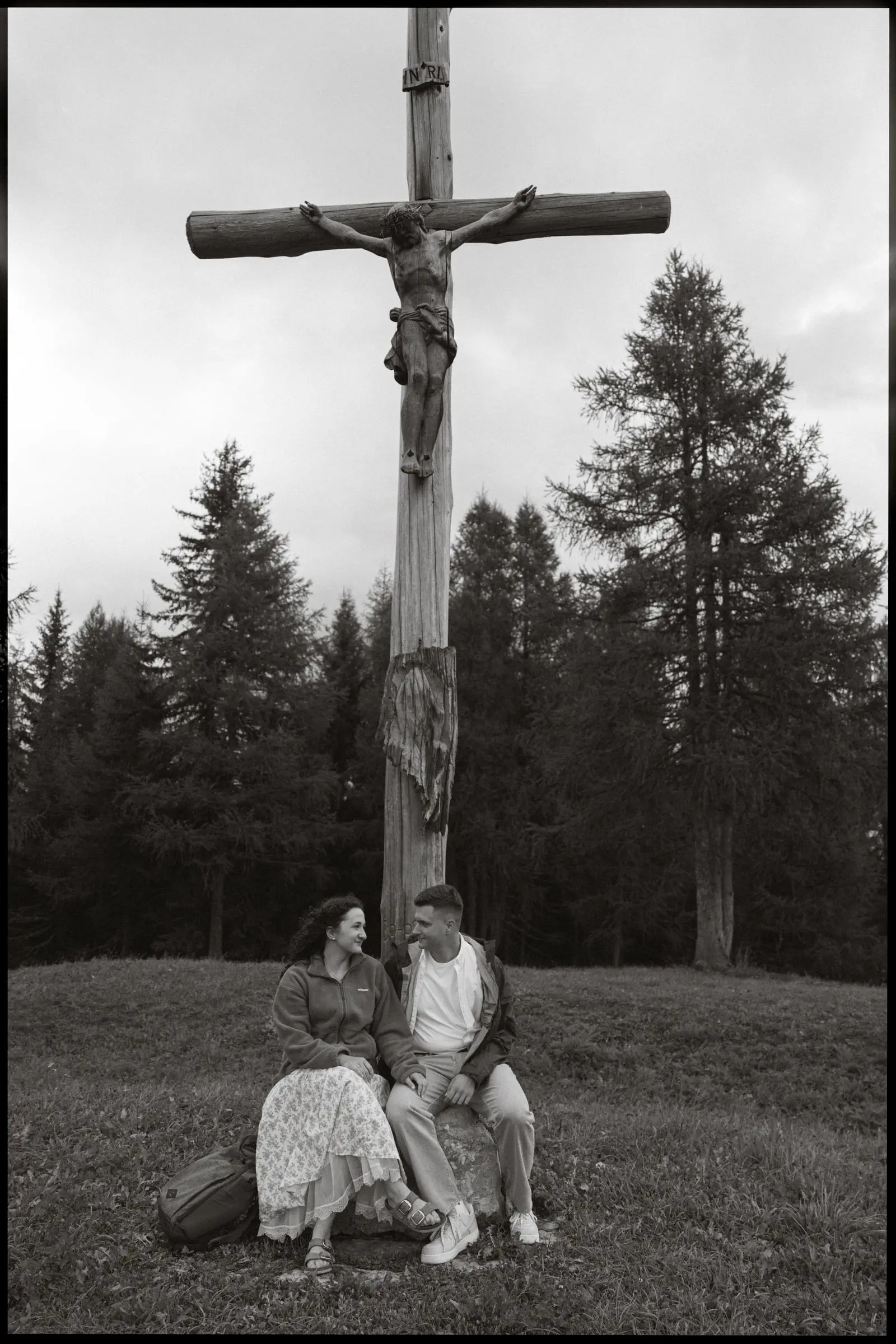 Black and white photo of the couple sitting under a large wooden crucifix