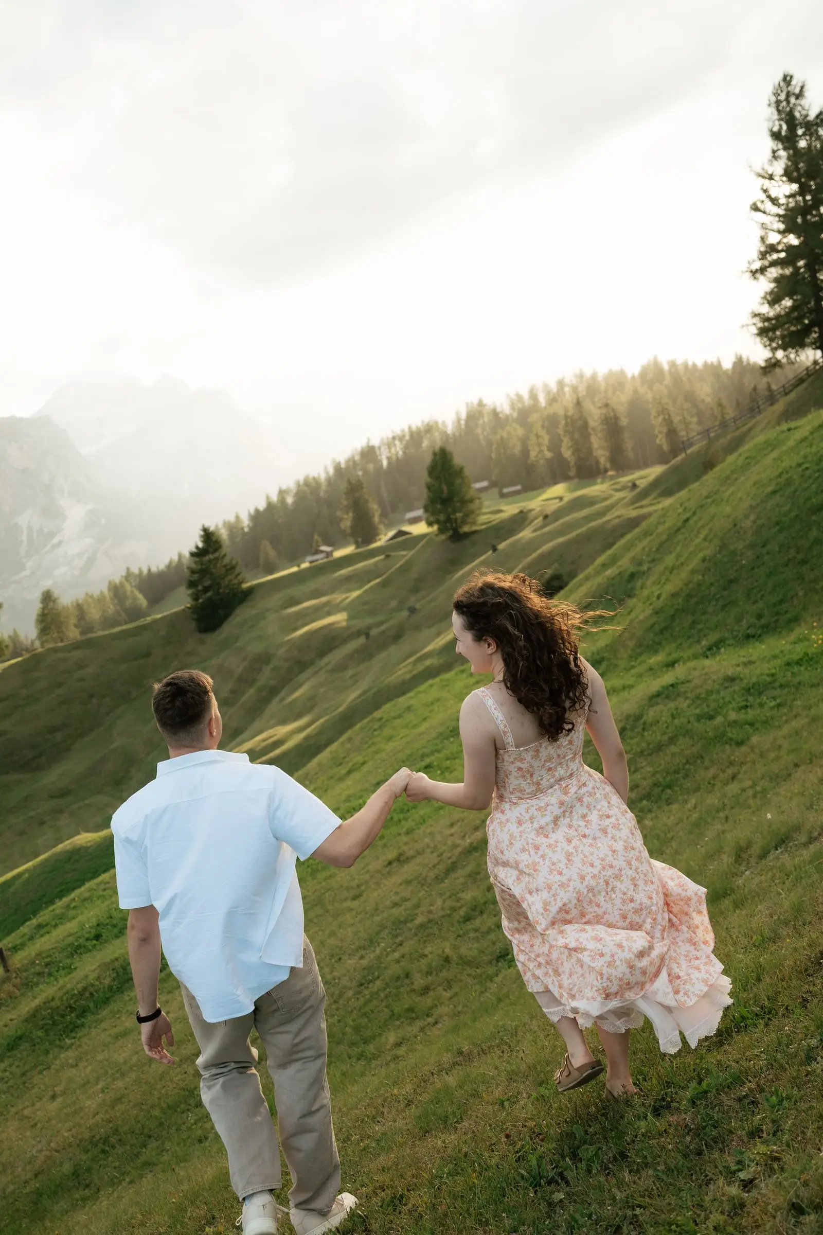 Couple running hand in hand up a meadow at golden hour