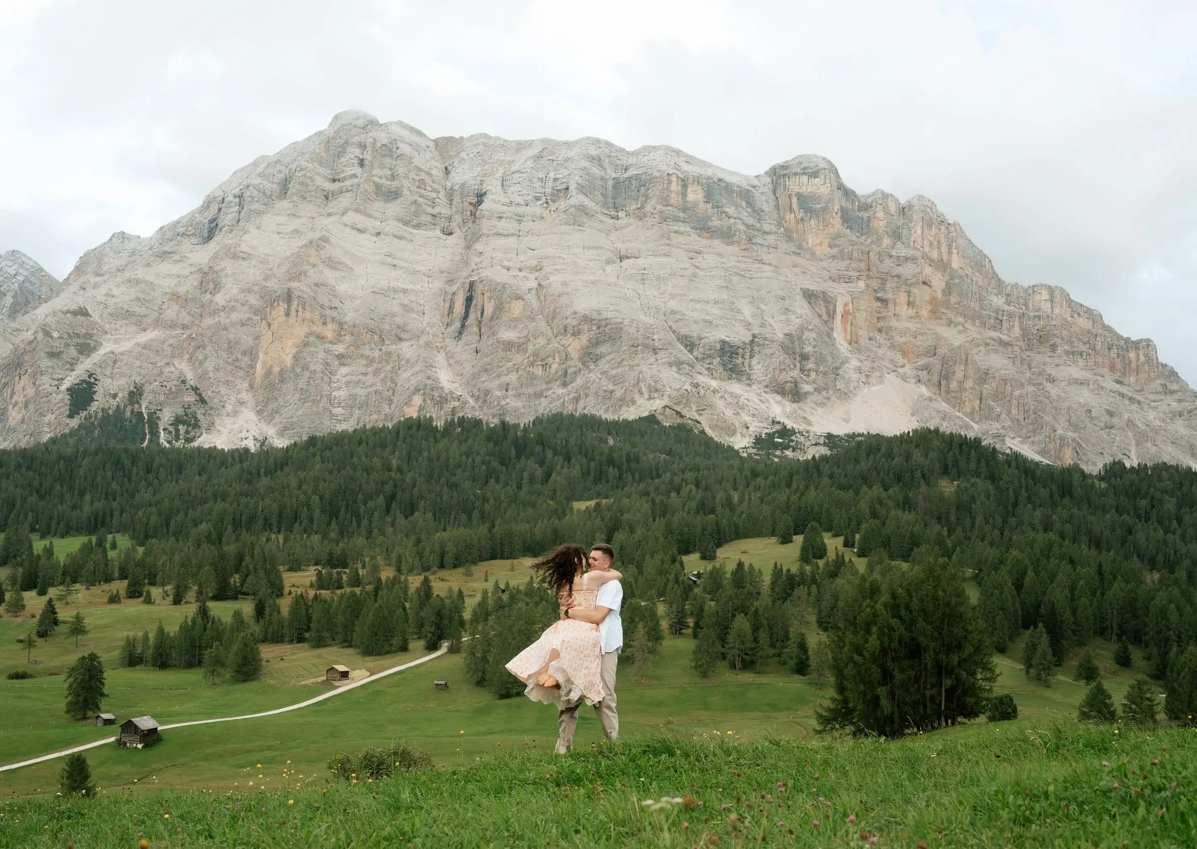 He lifts her in a wide meadow below the Sas dla Crusc rock wall