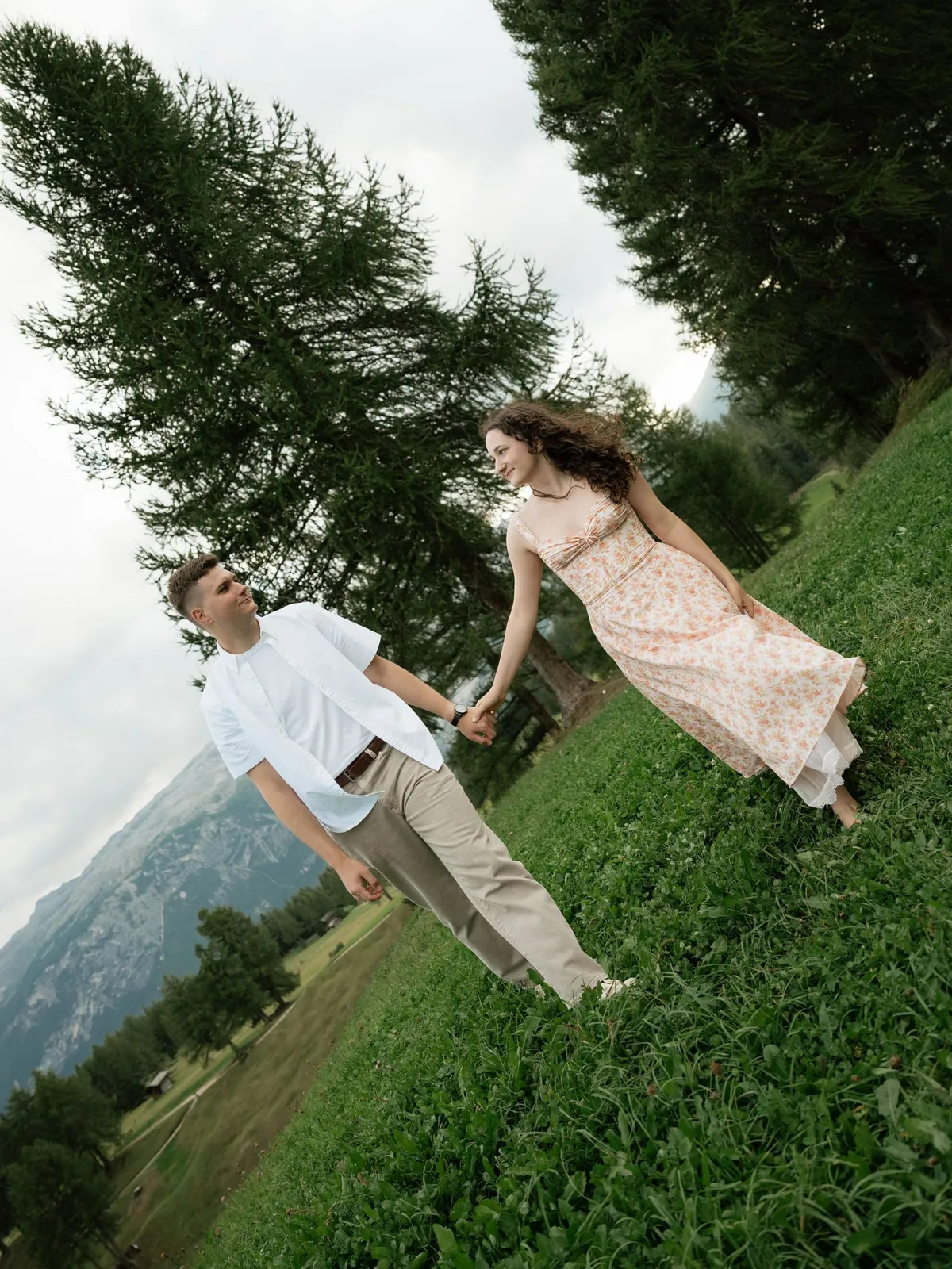 Couple walking hand in hand along a sloping meadow under larches