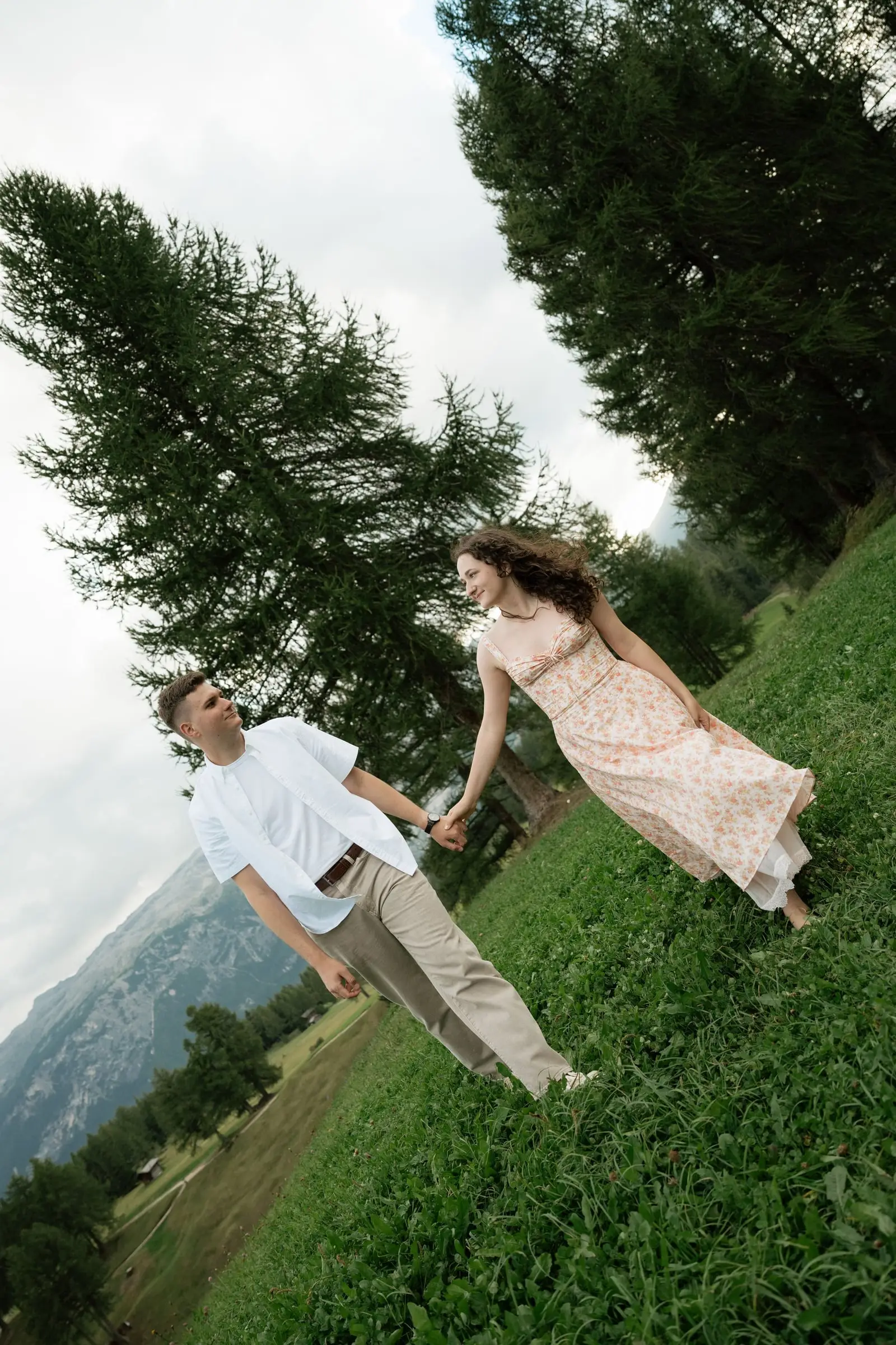 Couple walking hand in hand along a sloping meadow under larches
