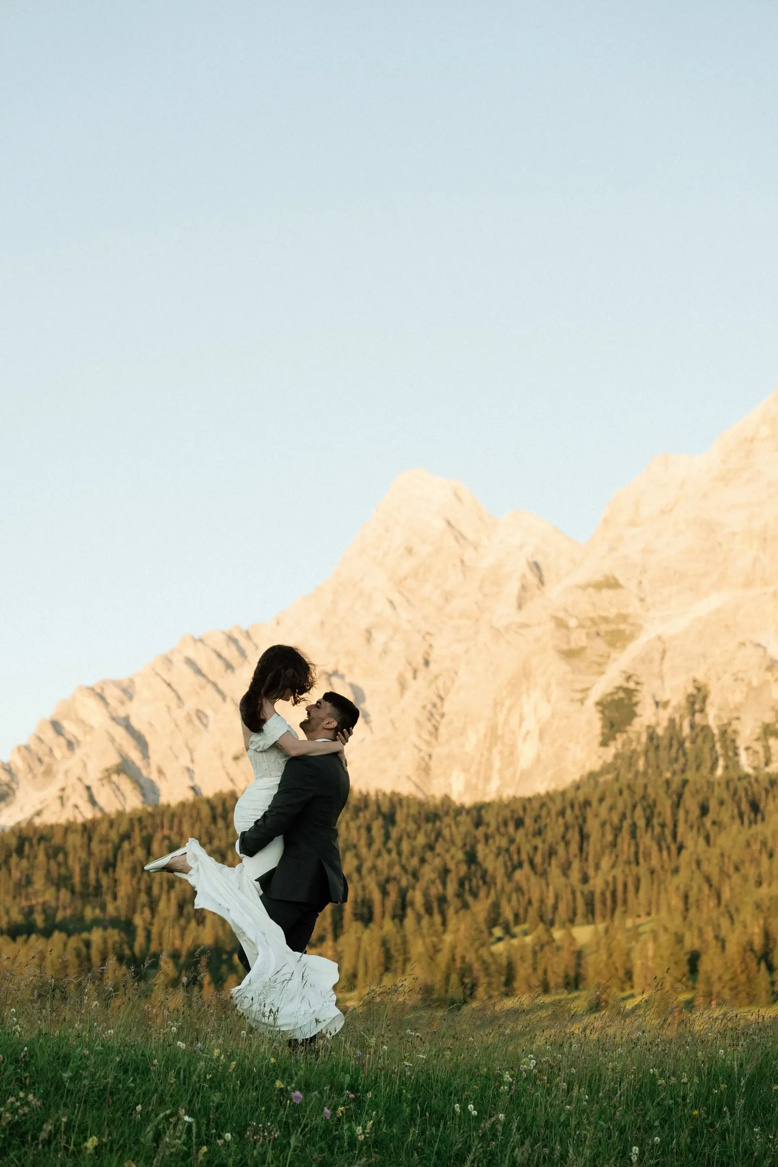 Groom spins the bride in a meadow below sunlit Dolomites peaks at La Val