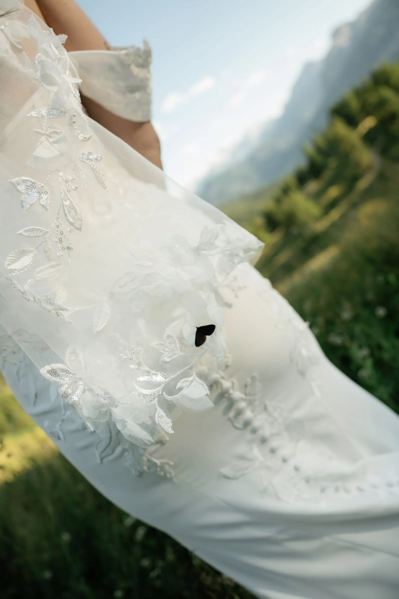Detail of the lace wedding gown blowing in the wind above the valley