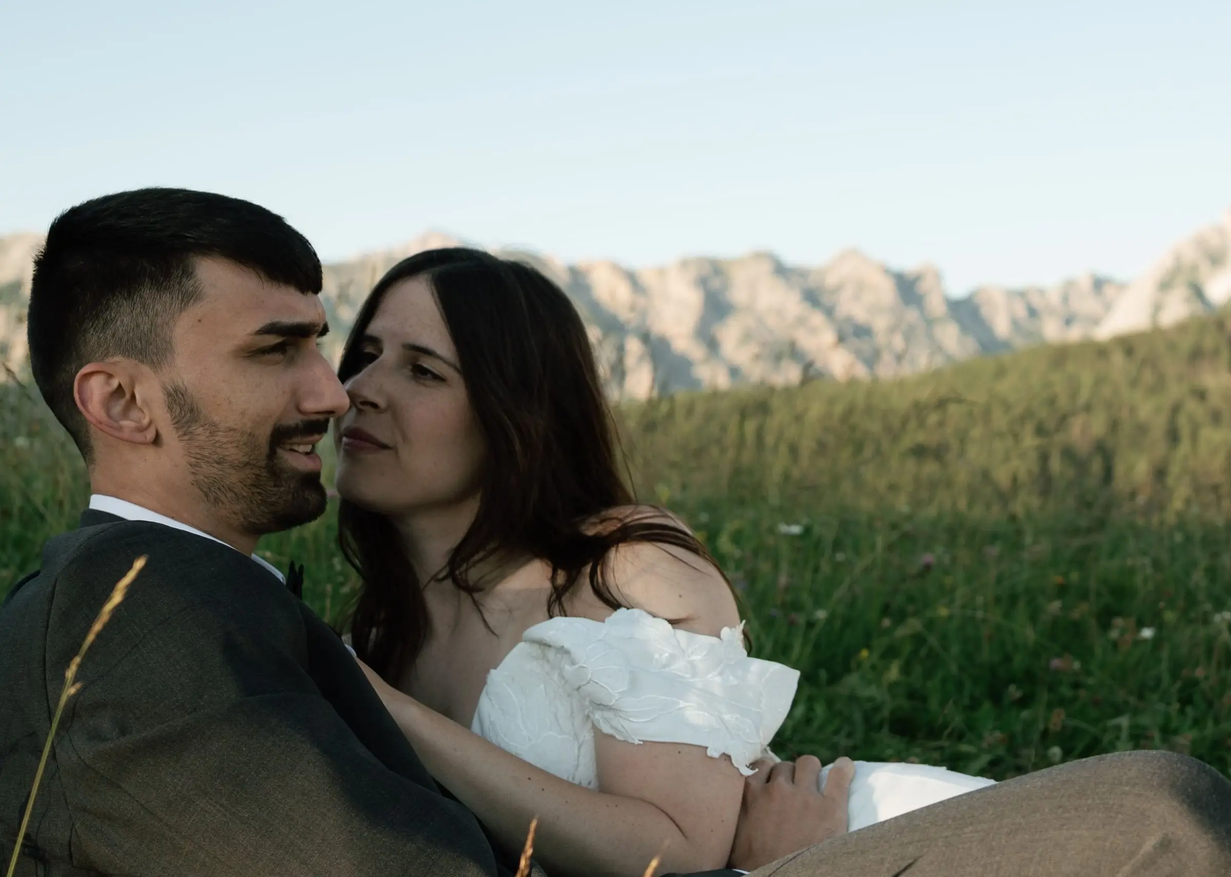 Bride and groom close together in the grass, mountains behind