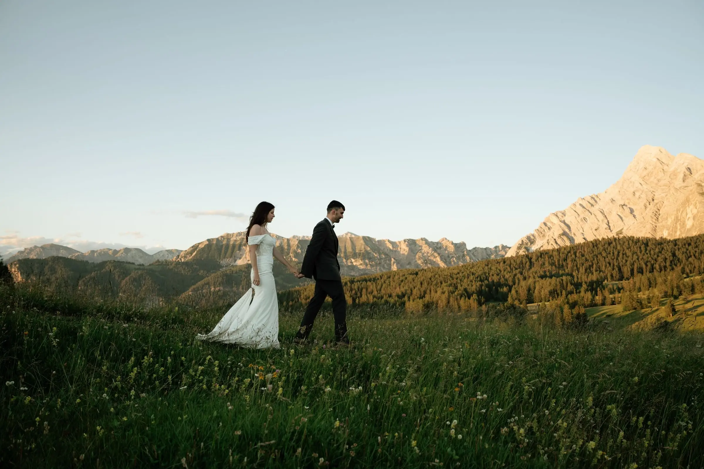 Bride and groom walking through a meadow at golden hour in Val Badia