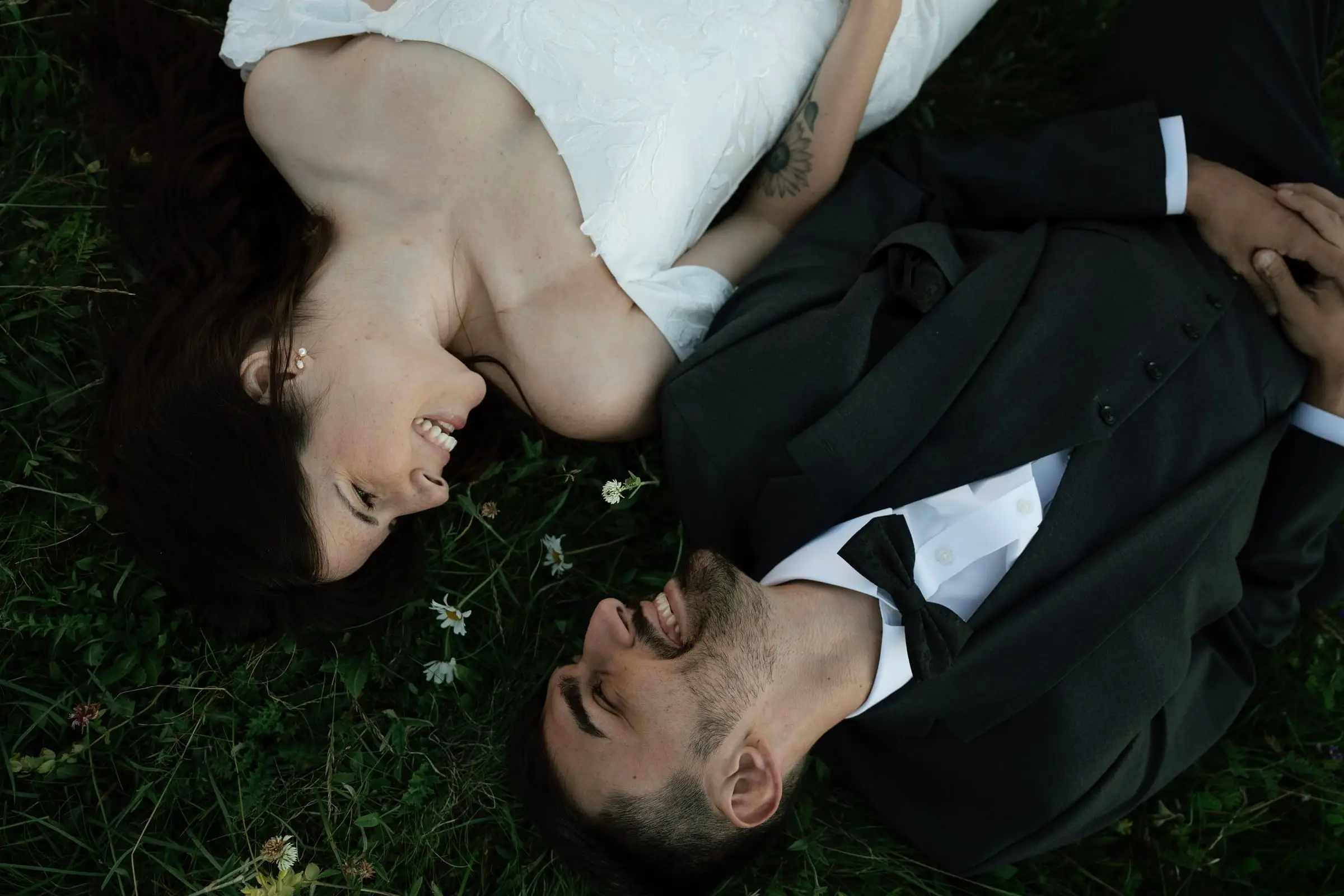 Bride and groom lying head to head in the grass, laughing