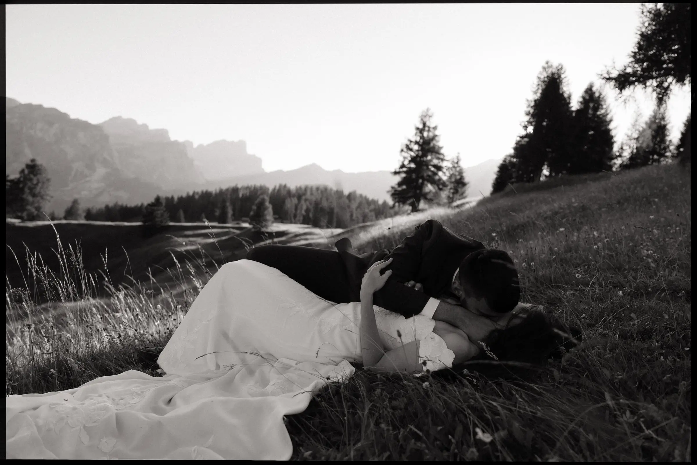 Black and white photo of the couple lying in the grass, kissing, on film