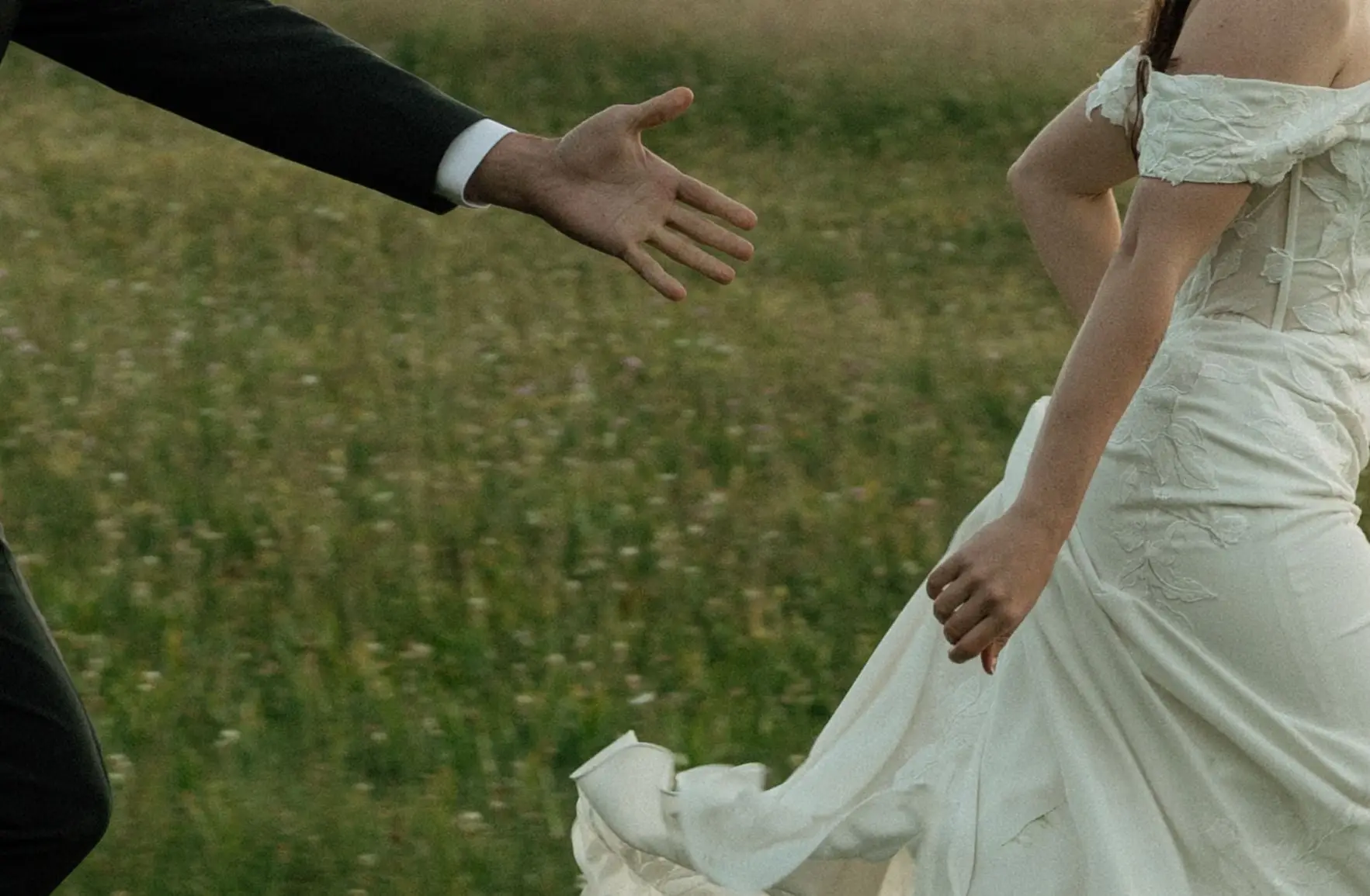 He reaches for her hand as she walks through the meadow in her gown