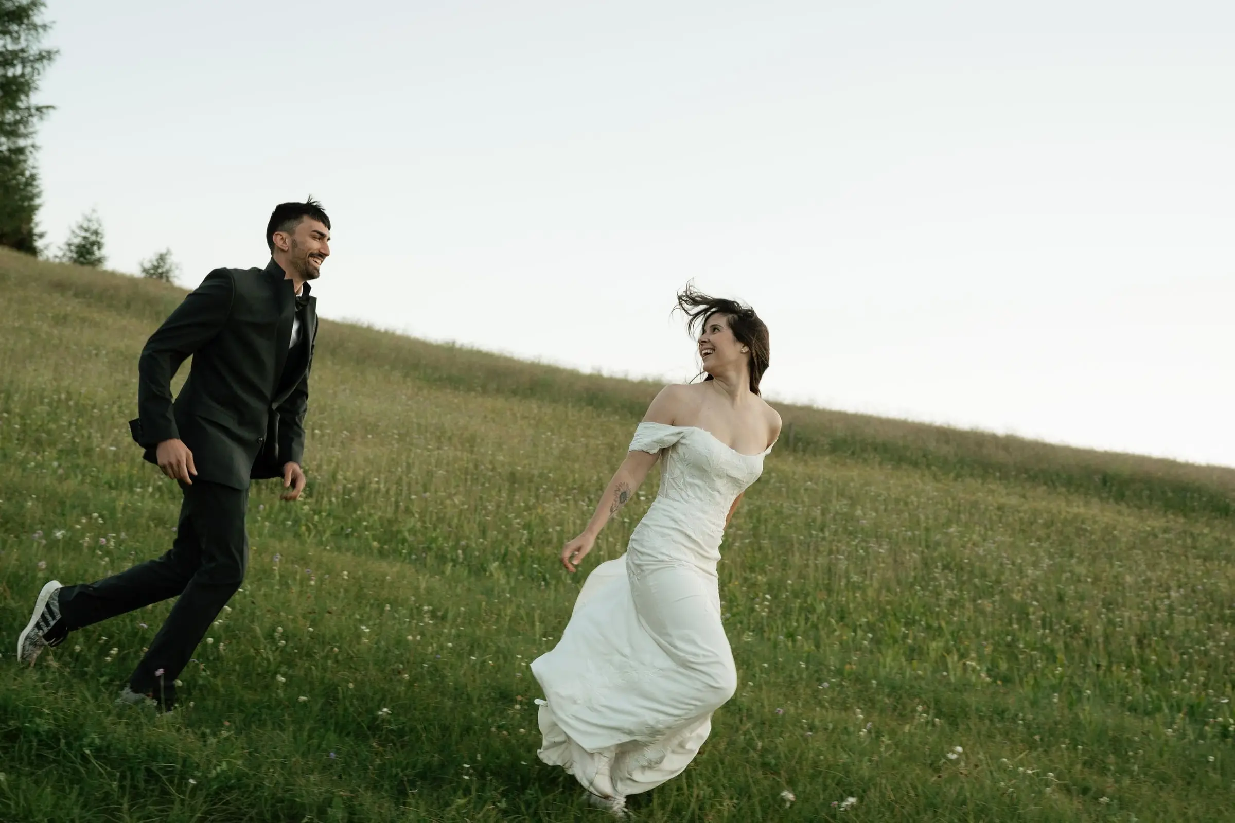 Groom running after the laughing bride across a steep meadow