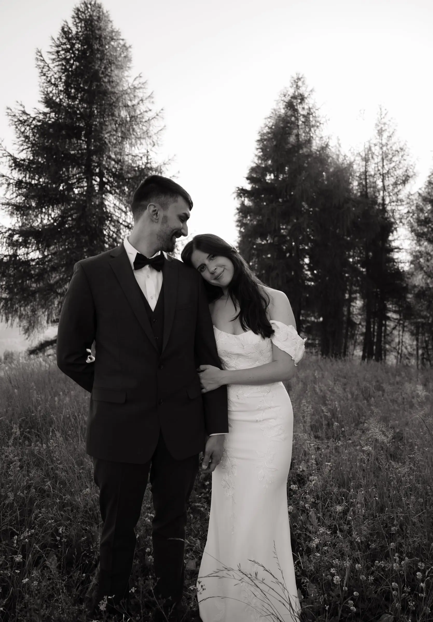 Black and white photo of the bride leaning on the groom among larches