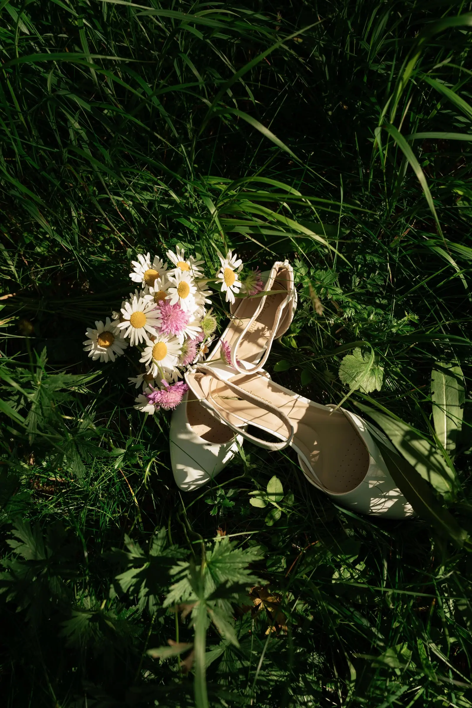 Wedding shoes and a daisy bouquet lying in the grass