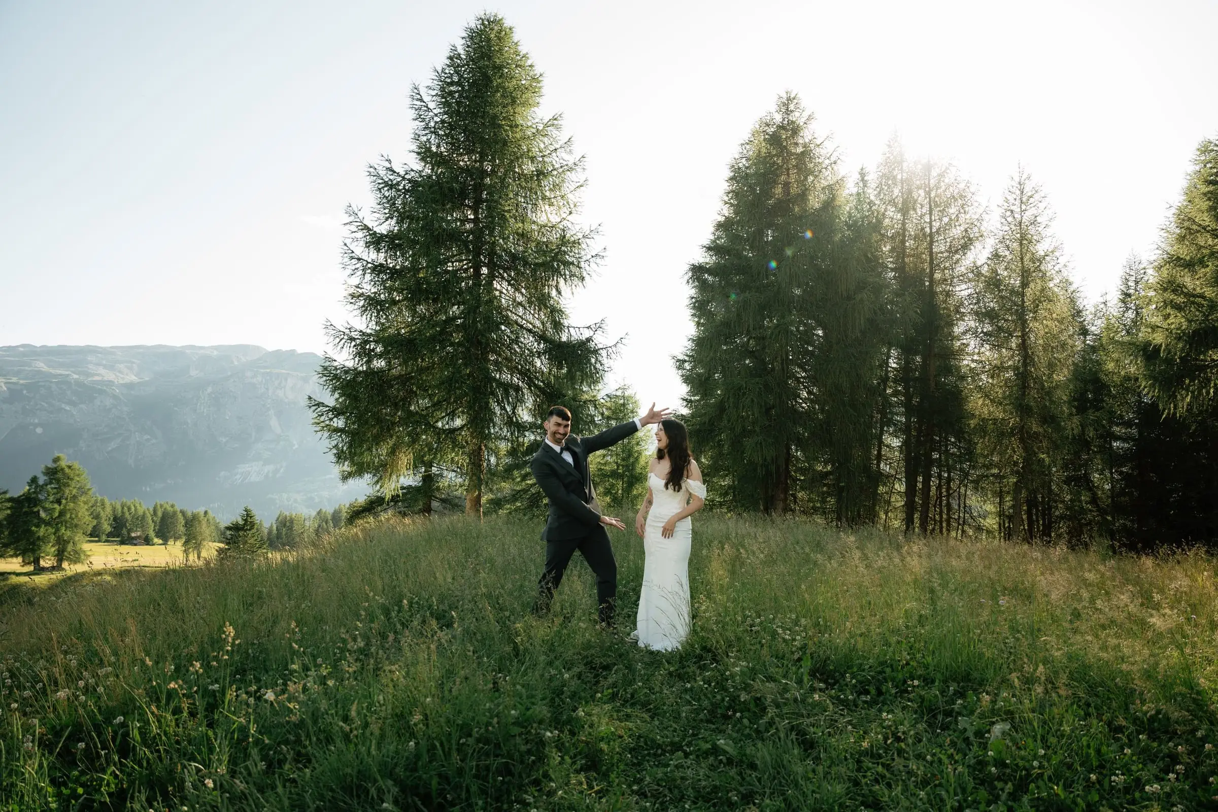 Groom twirls the bride under tall larches in the evening light