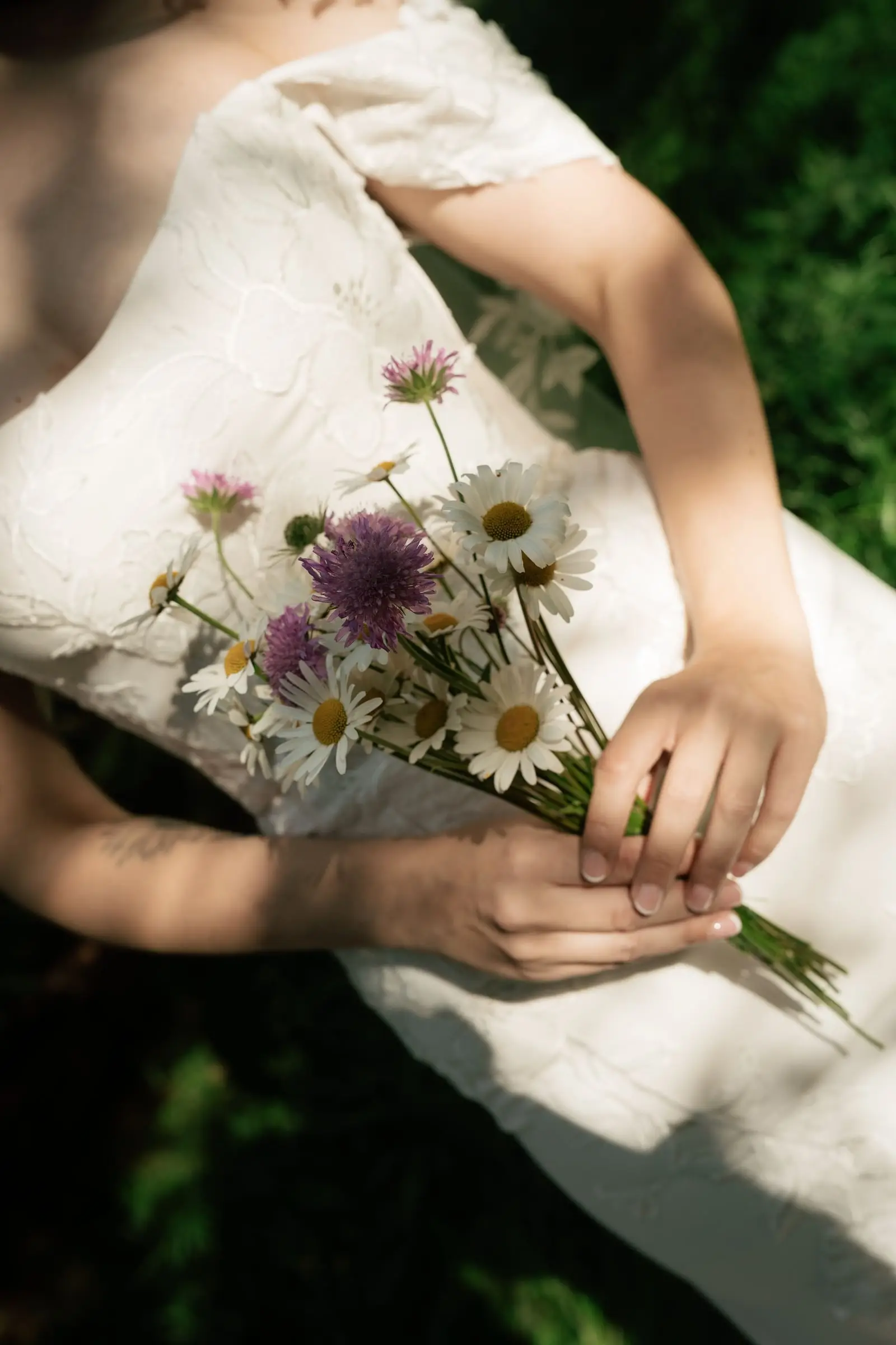 Bride holding a bouquet of daisies and purple wildflowers