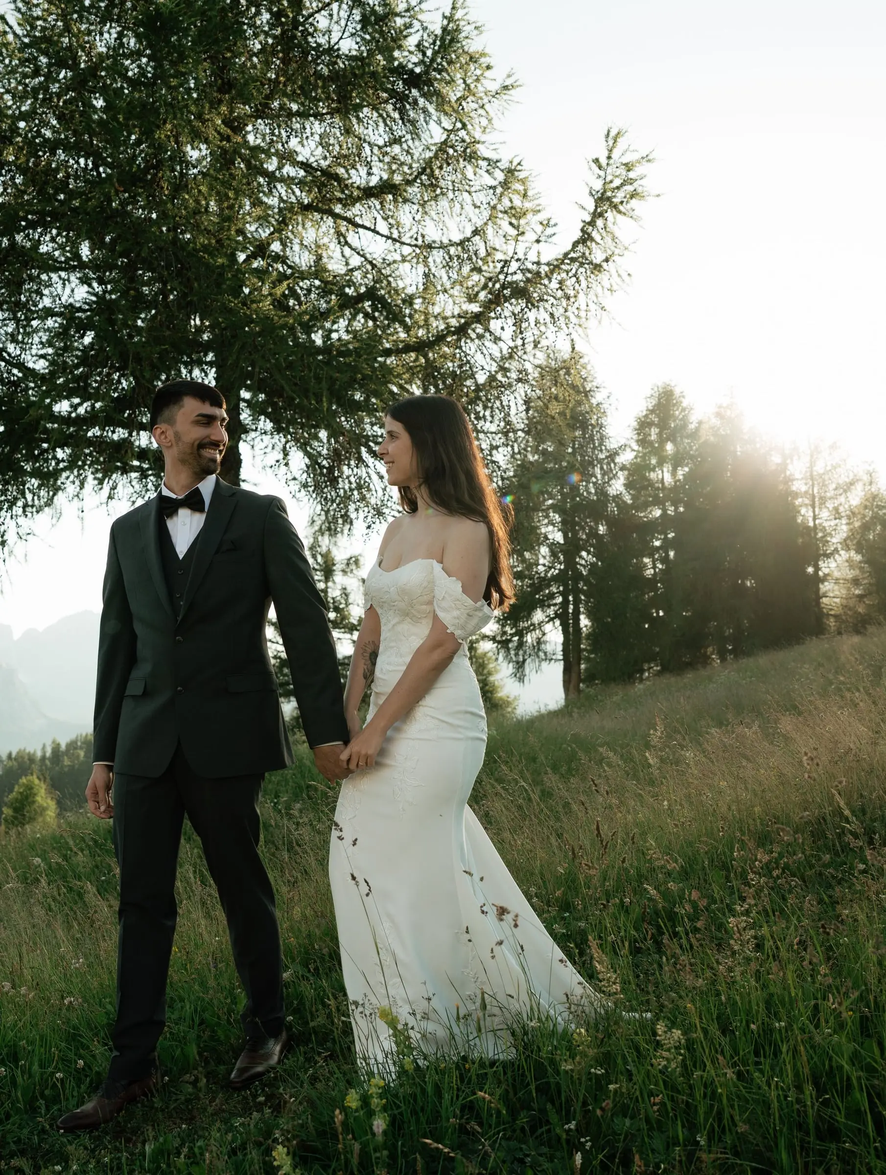 Bride and groom holding hands in sunlight under a larch