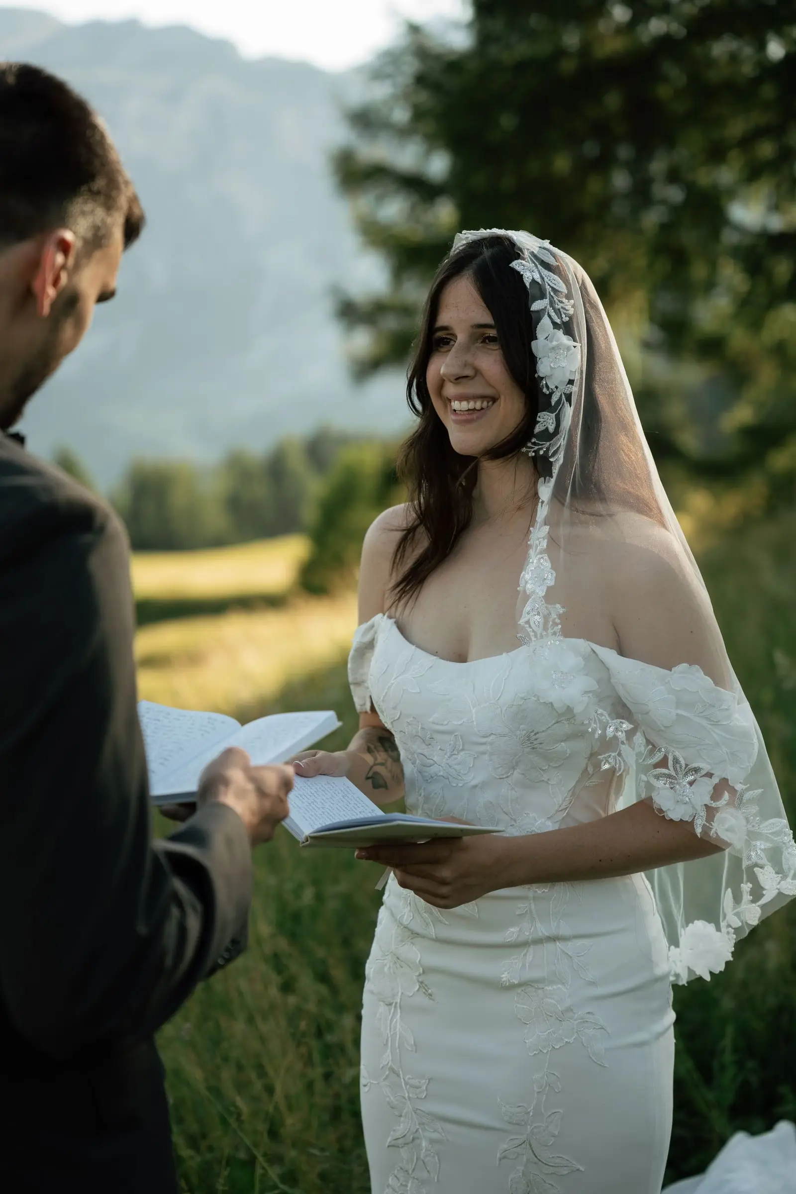 Smiling bride in a lace veil reading her vows