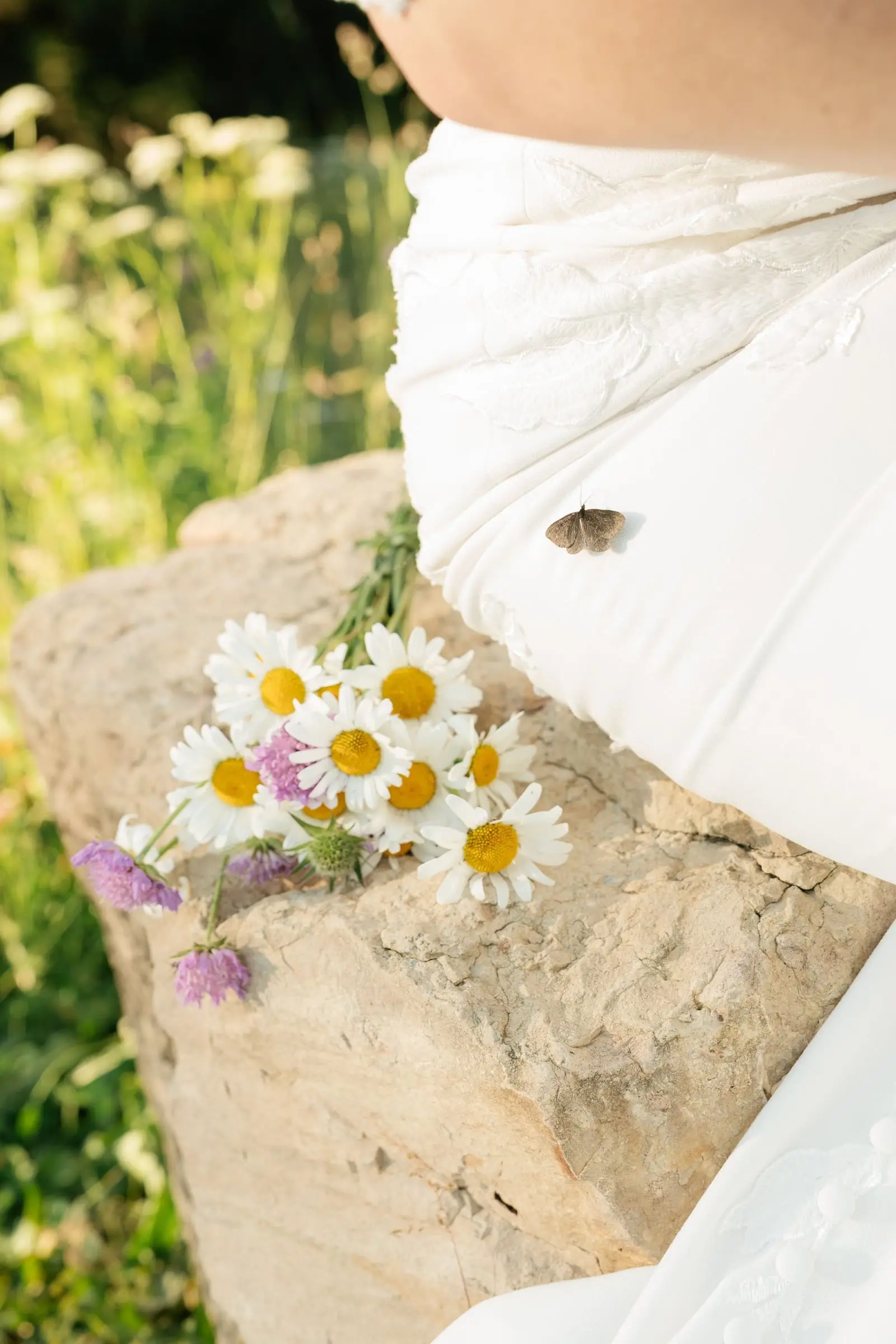 Daisy bouquet on a rock with a small butterfly on the wedding gown