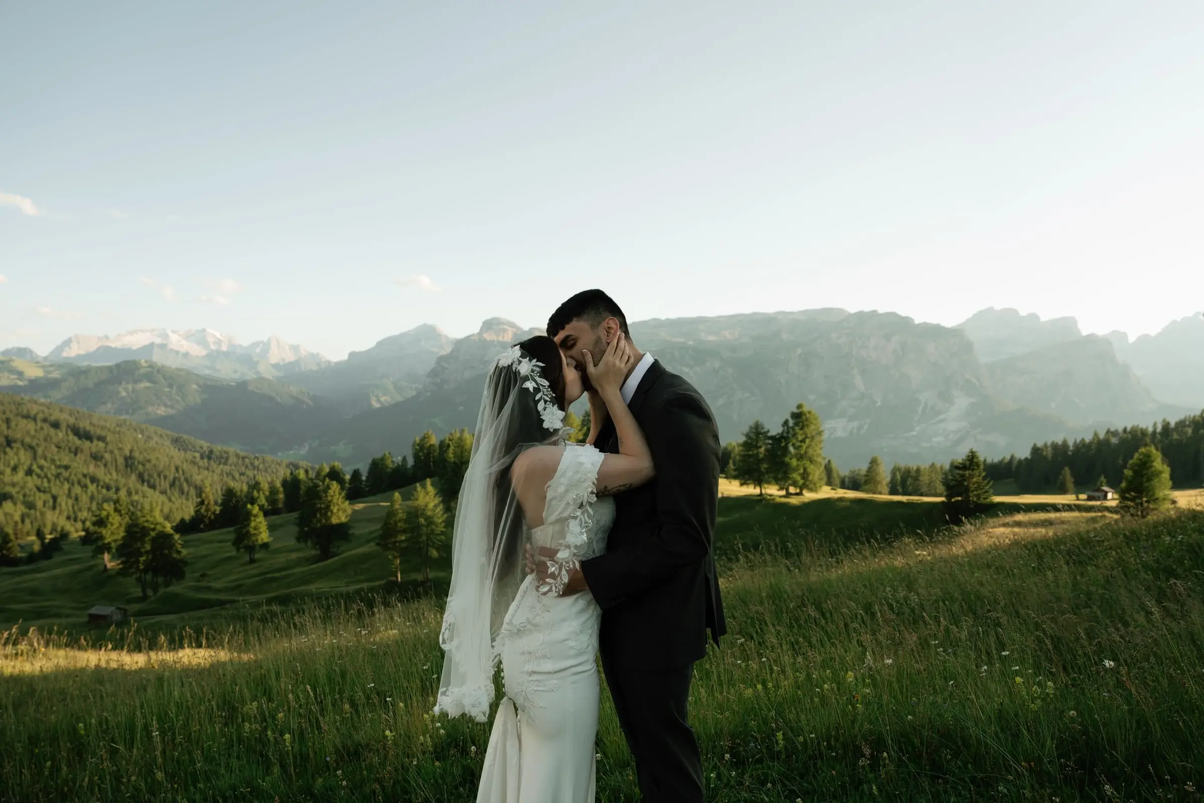 Bride and groom kissing in a meadow with mountains on the horizon