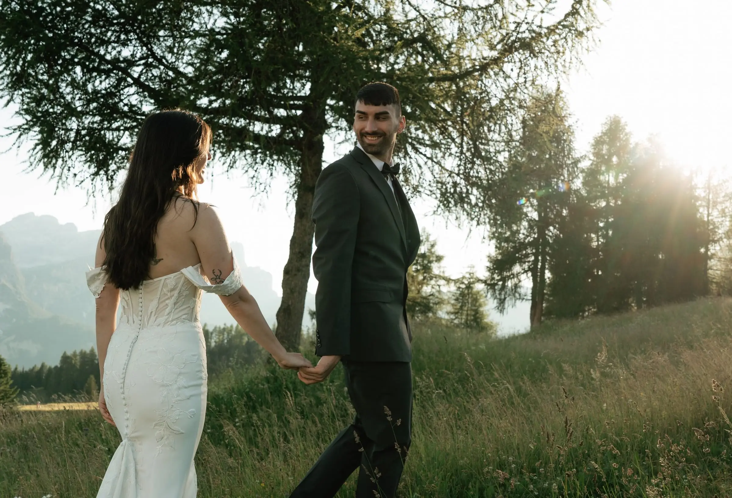 Bride leads the groom by the hand under a larch at golden hour