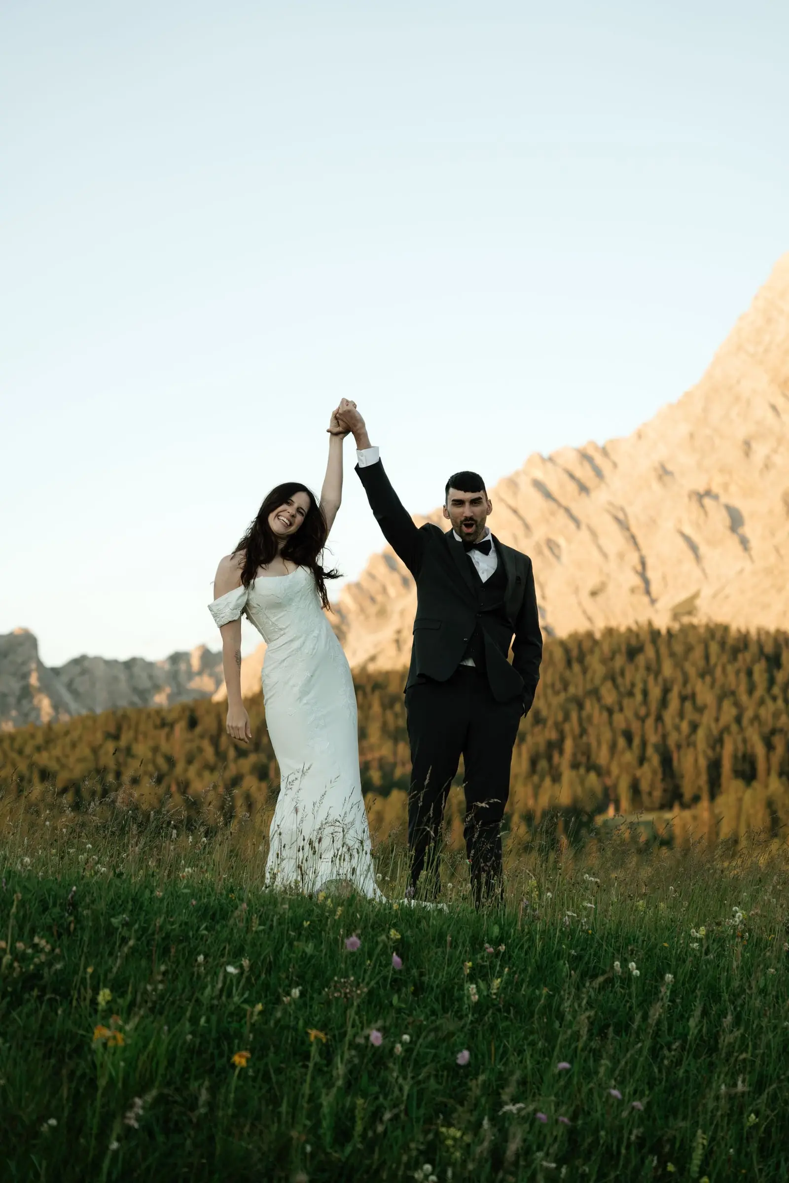 Bride and groom raise their joined hands in celebration against the mountains
