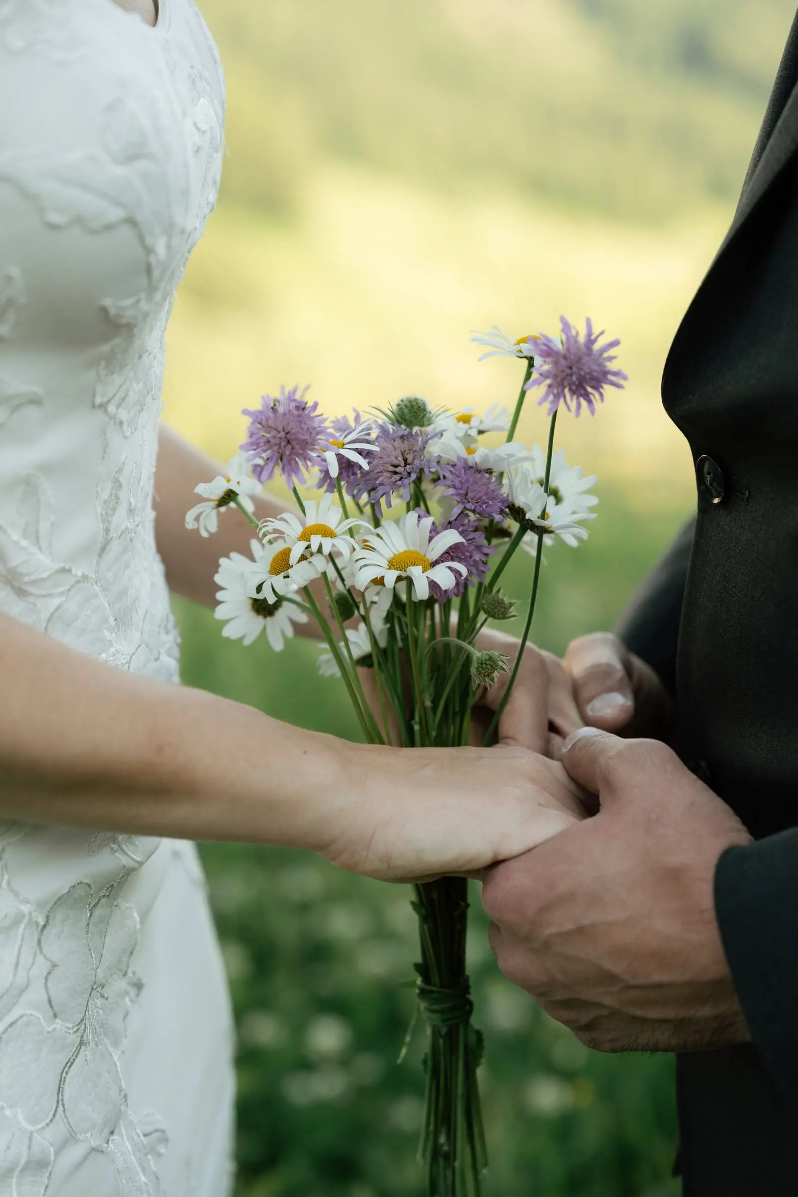 Close-up of joined hands and a bouquet of daisies and knapweed