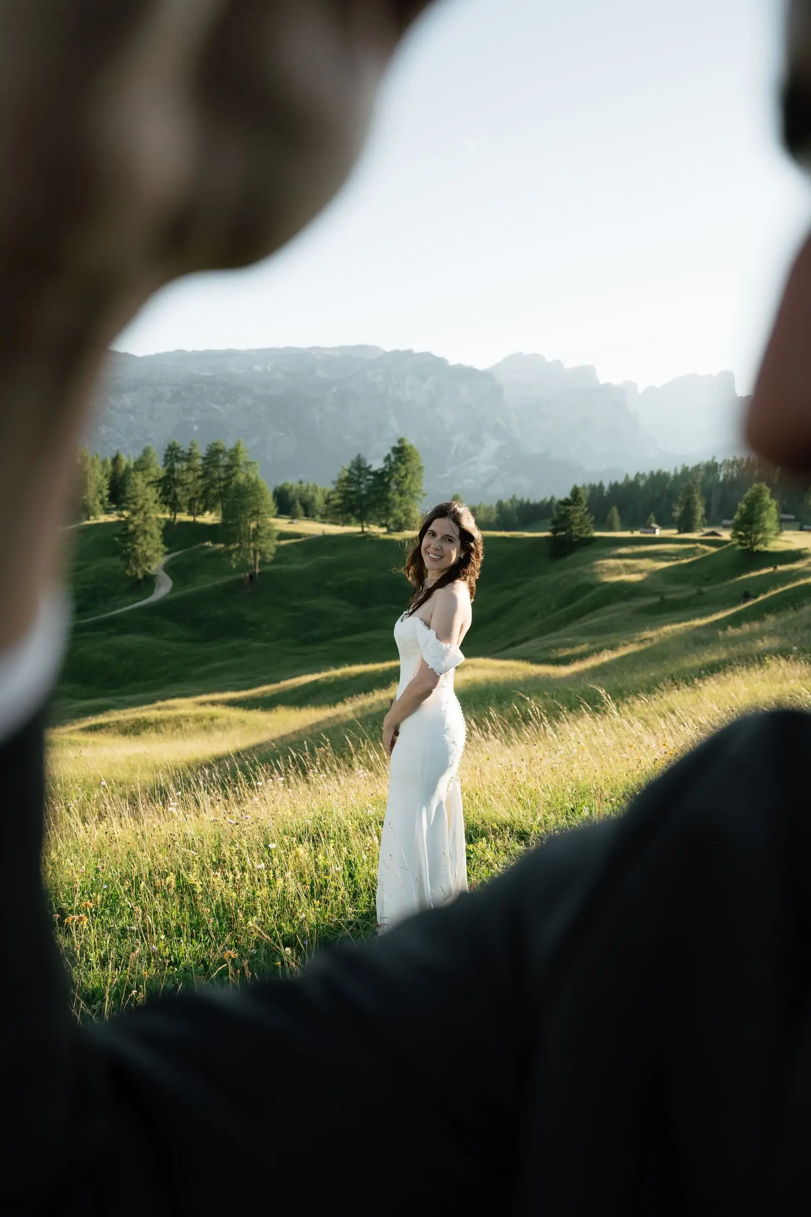 Bride in the meadow seen through the groom's arms
