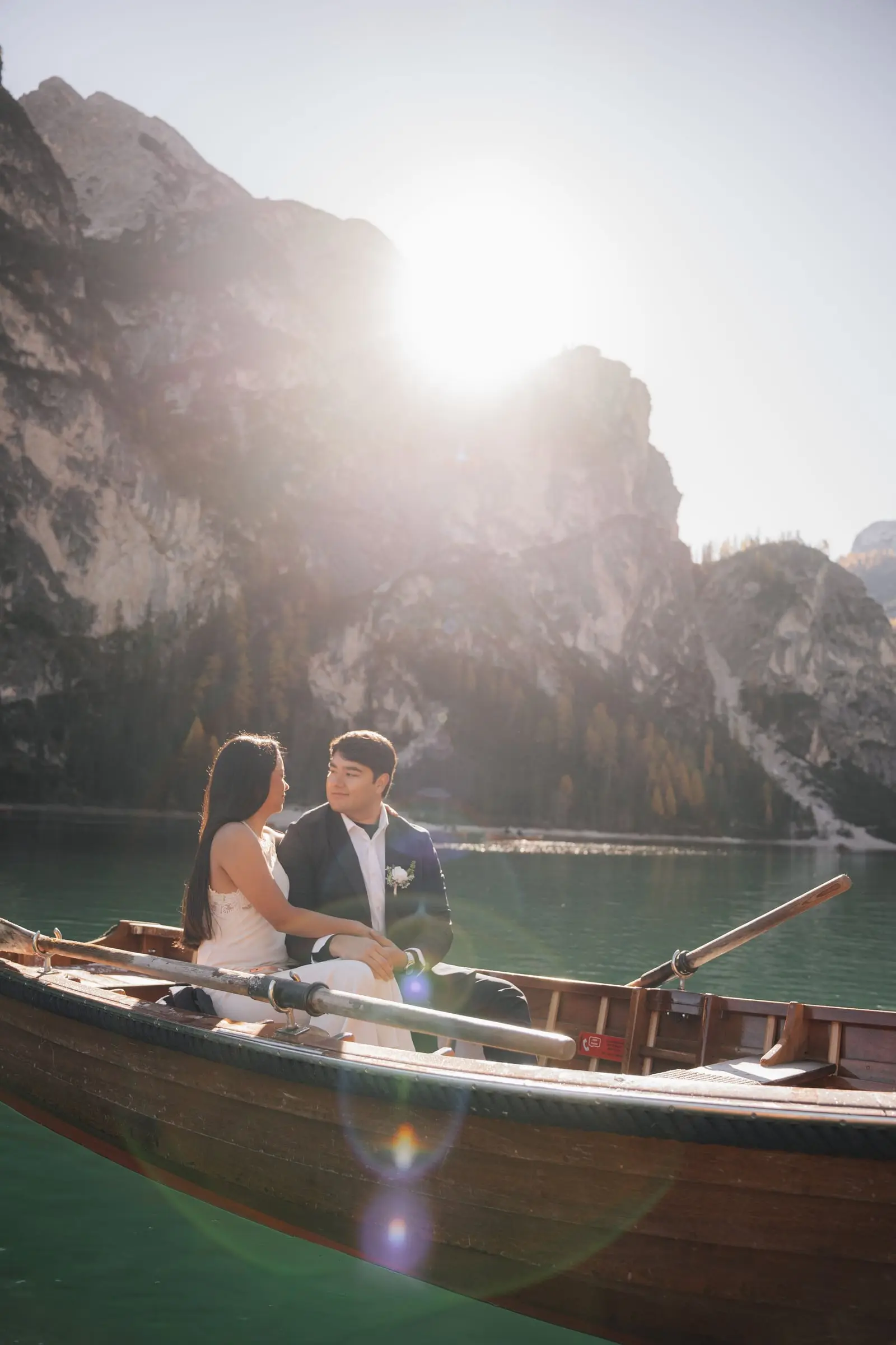 Couple in a wooden rowing boat on Lago di Braies with the sun over the peaks
