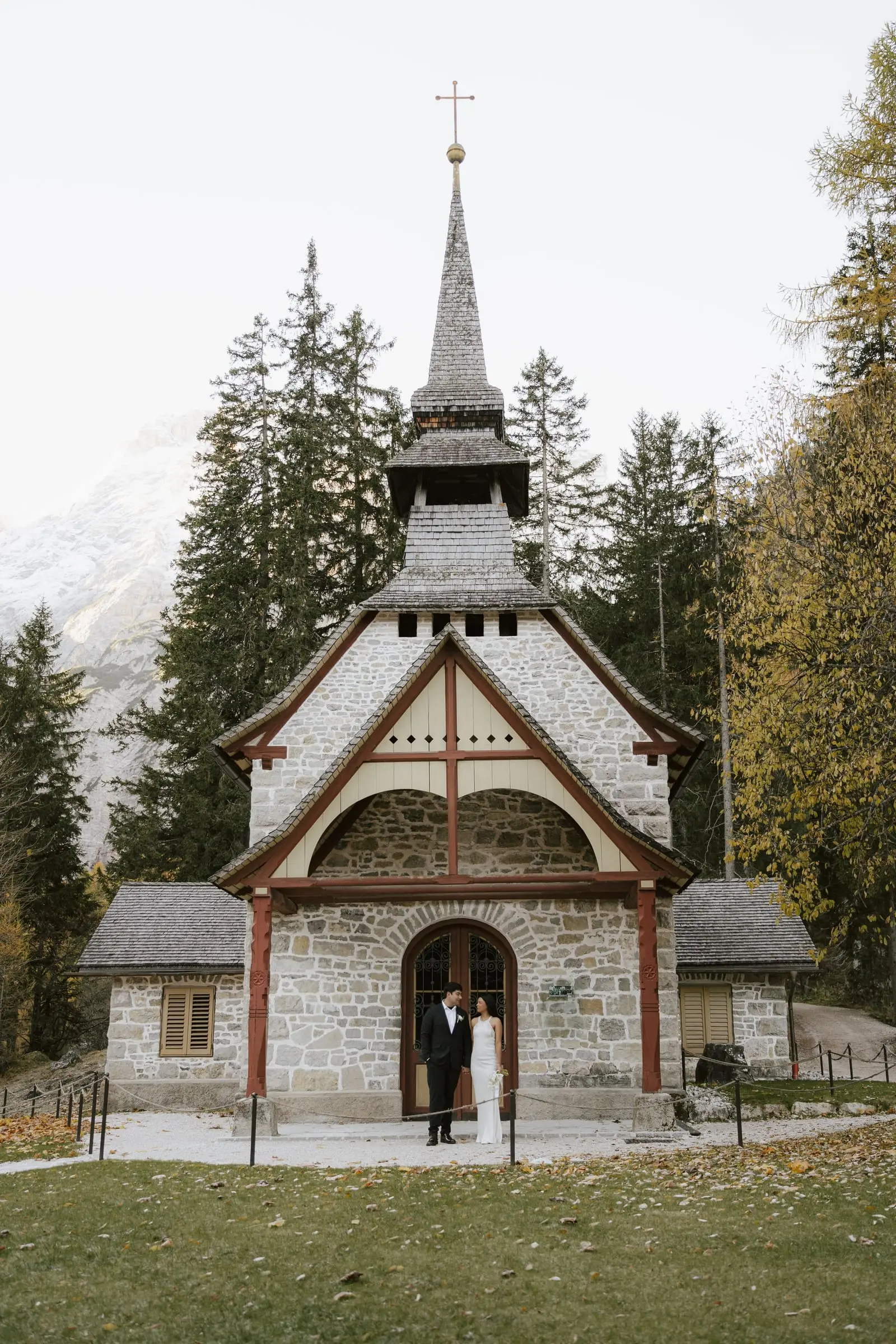 Couple at the door of the little stone chapel at Lago di Braies in autumn