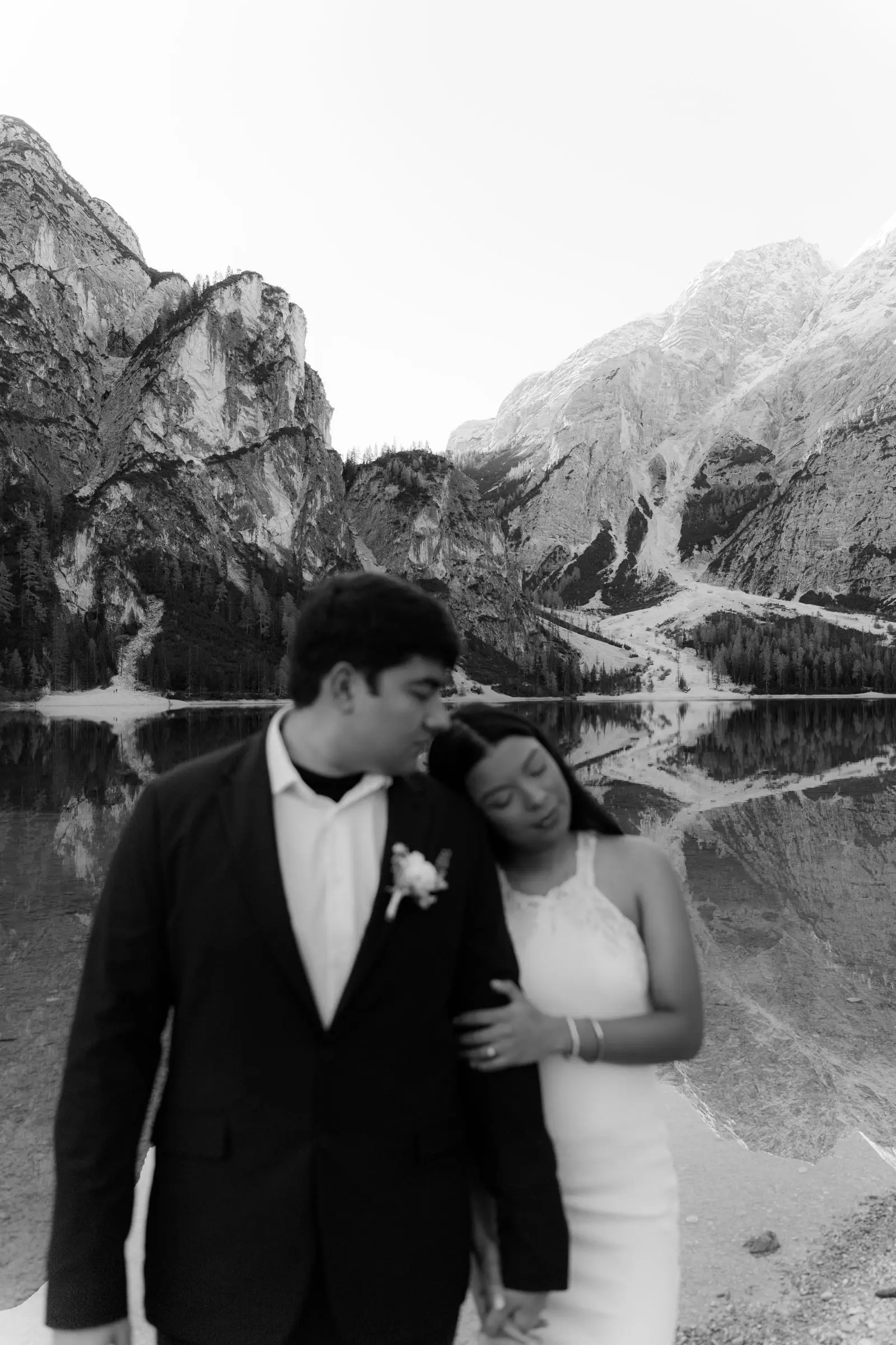 Black and white photo of the couple by the lake, mountains reflected in the water