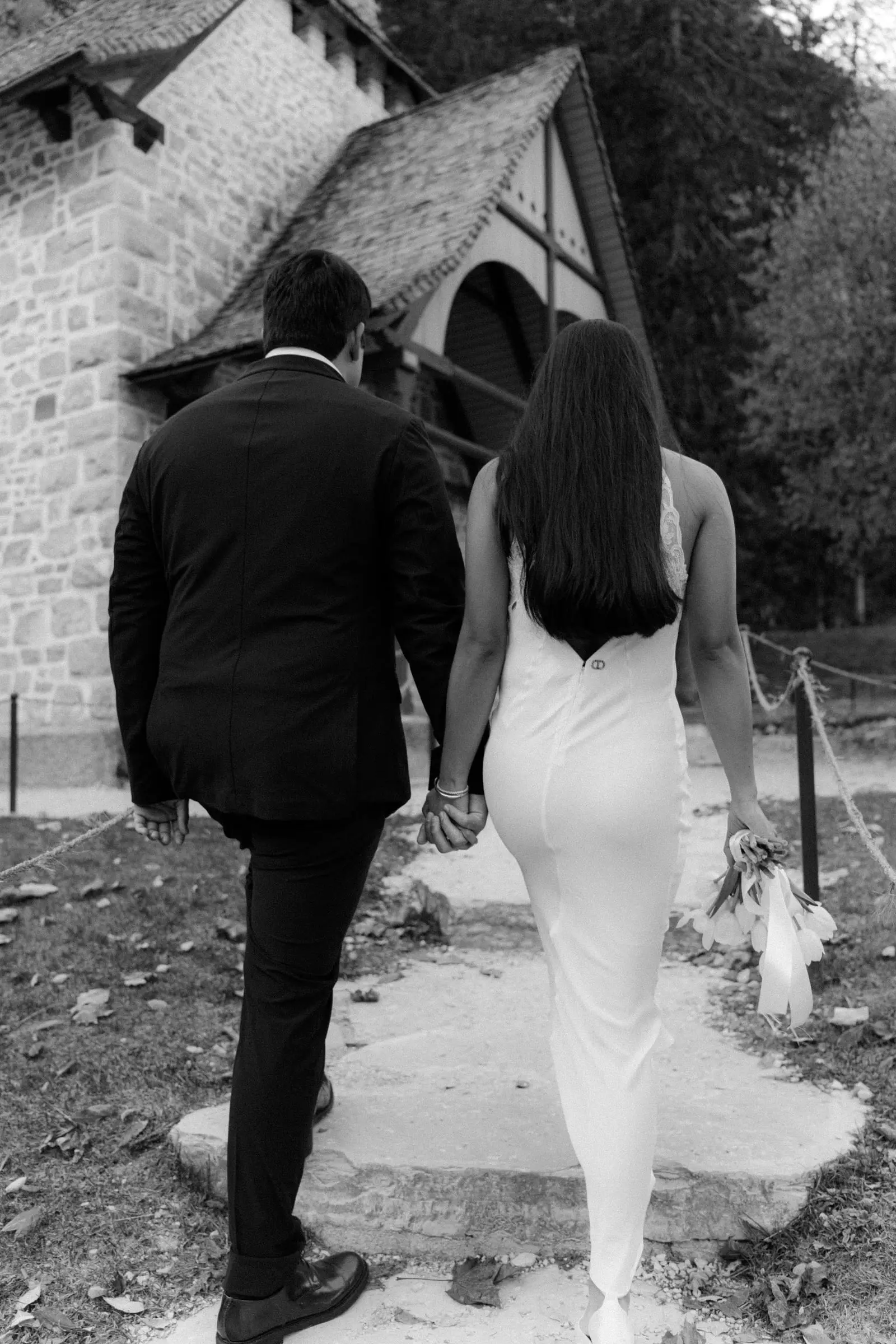 Black and white photo of the couple walking hand in hand to the lake chapel