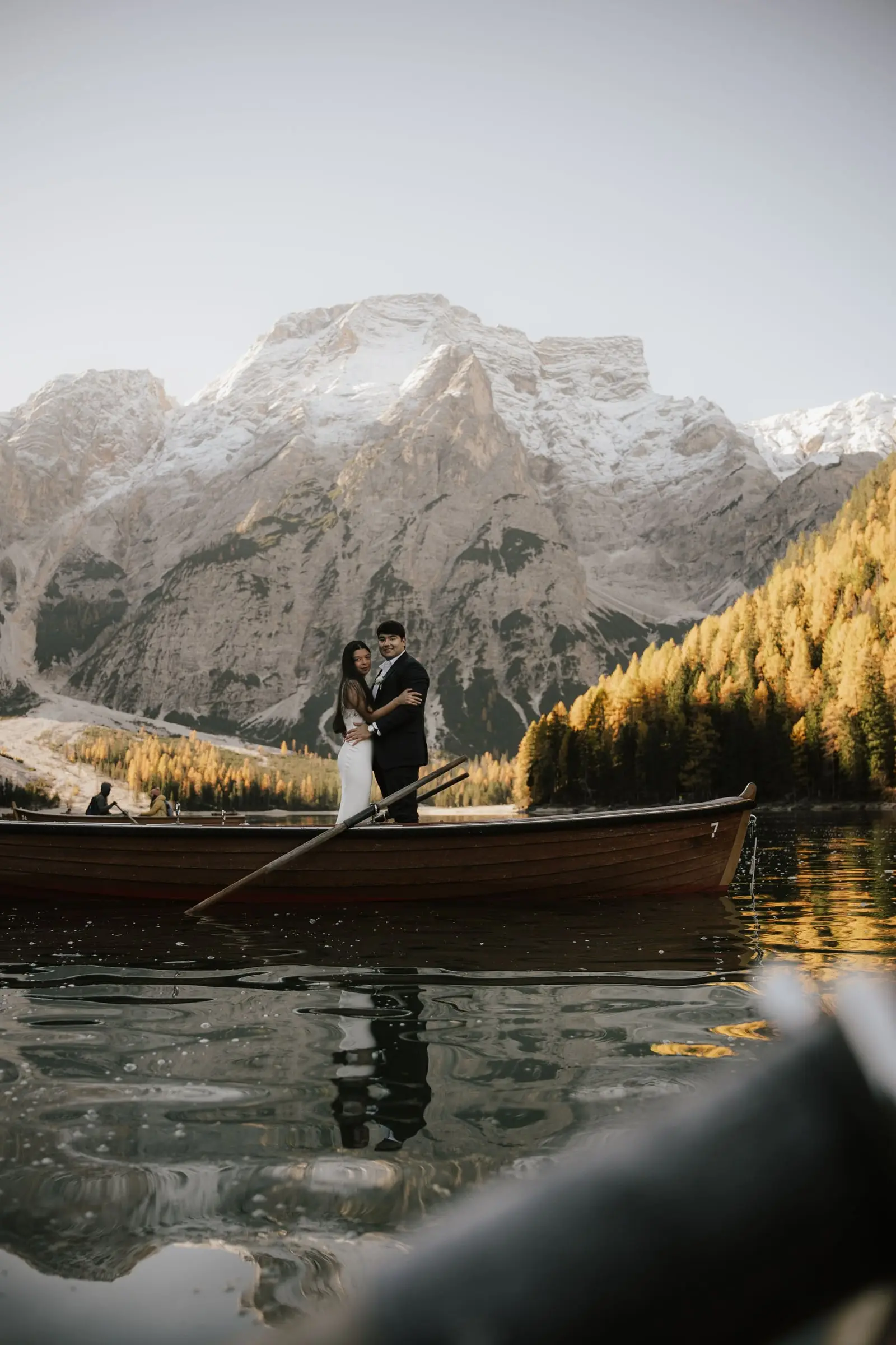 Couple standing in a boat on the mirror-still lake, snowy peaks above