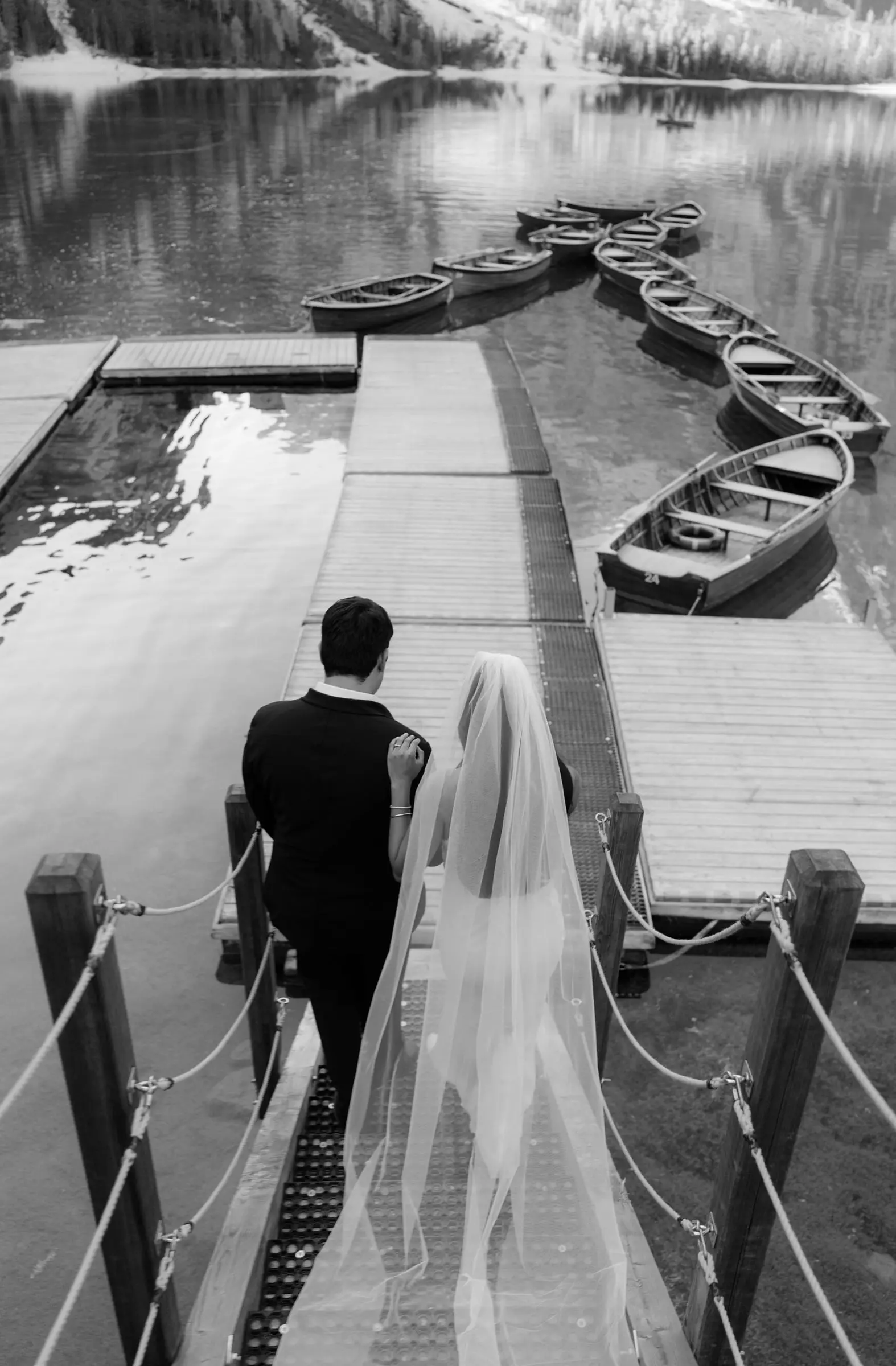 Black and white photo of the couple walking down the jetty past the wooden boats