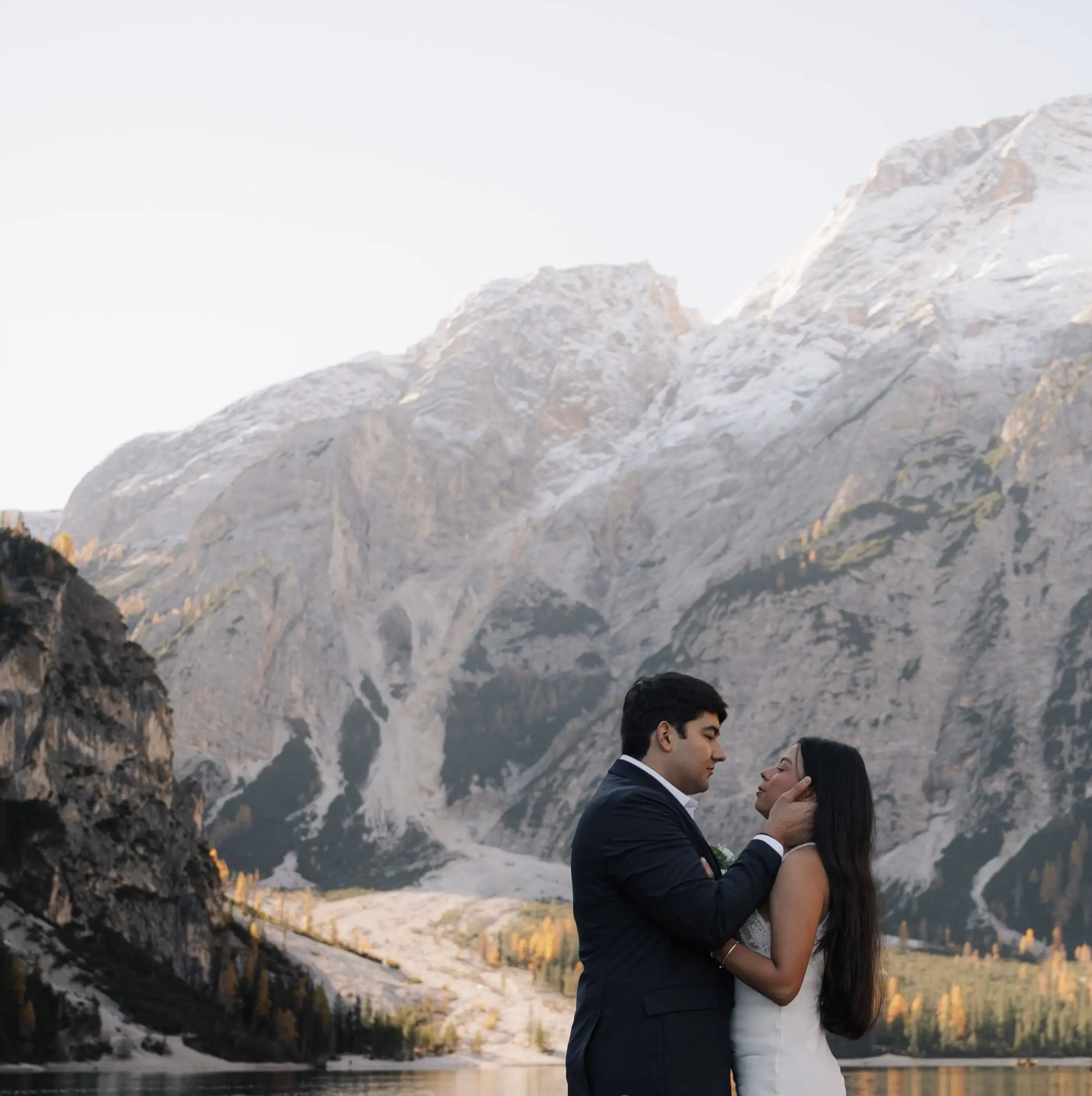 Couple face to face on the lake shore below snowy mountains