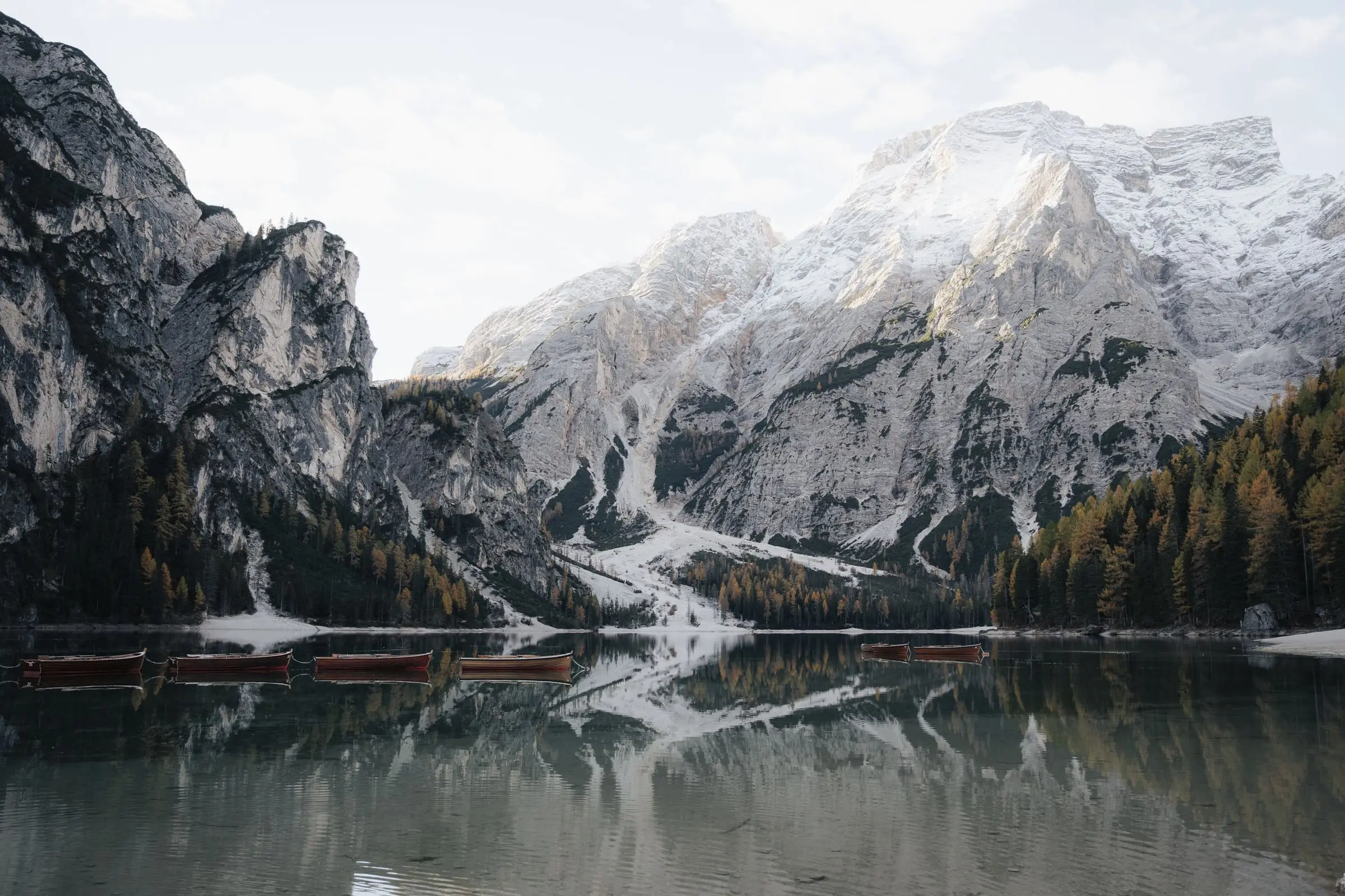 Lago di Braies with its wooden boats and snow-dusted peaks reflected in autumn