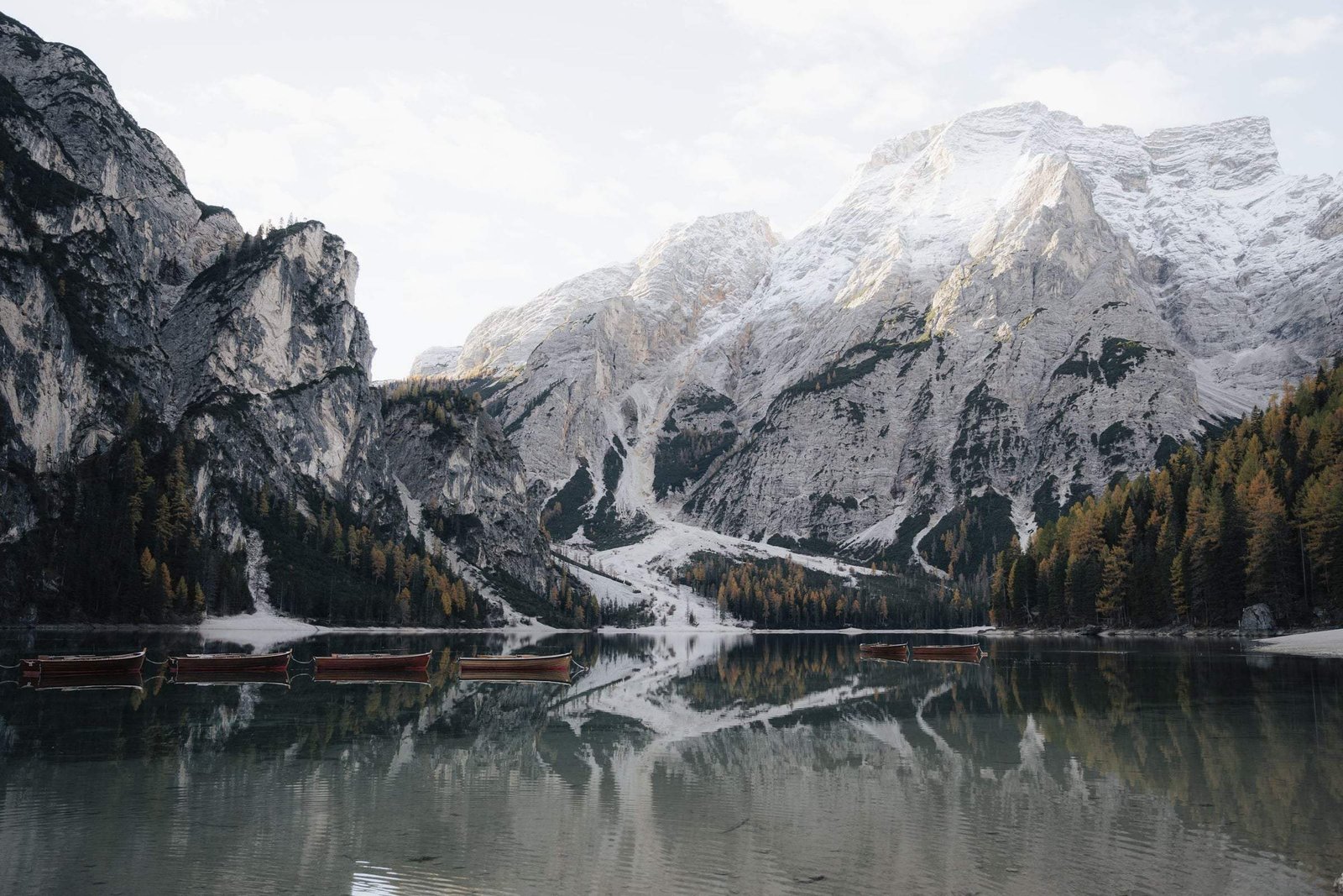 Lago di Braies with its wooden boats and snow-dusted peaks reflected in autumn