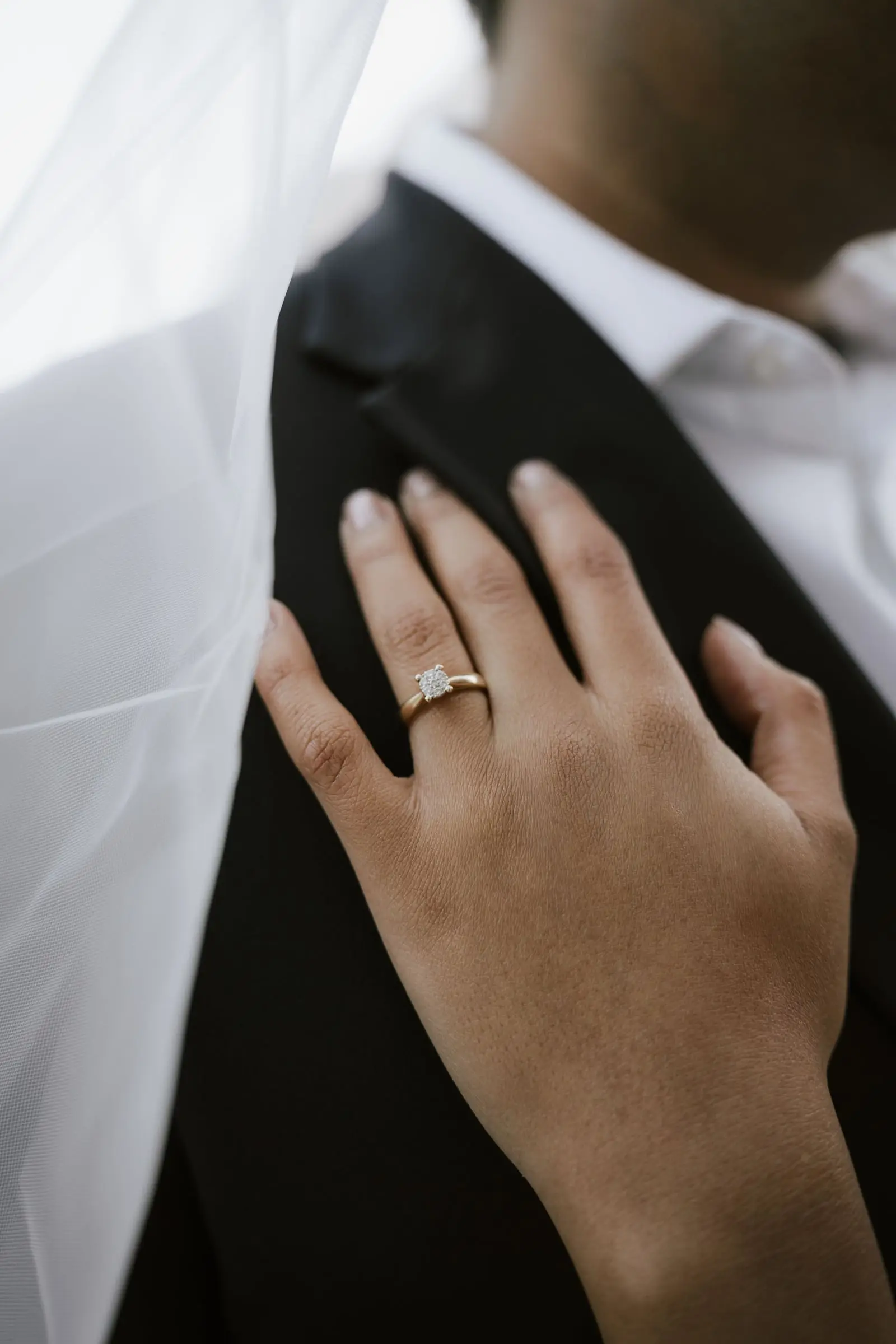 Her hand with an engagement ring on his dark suit, under the veil