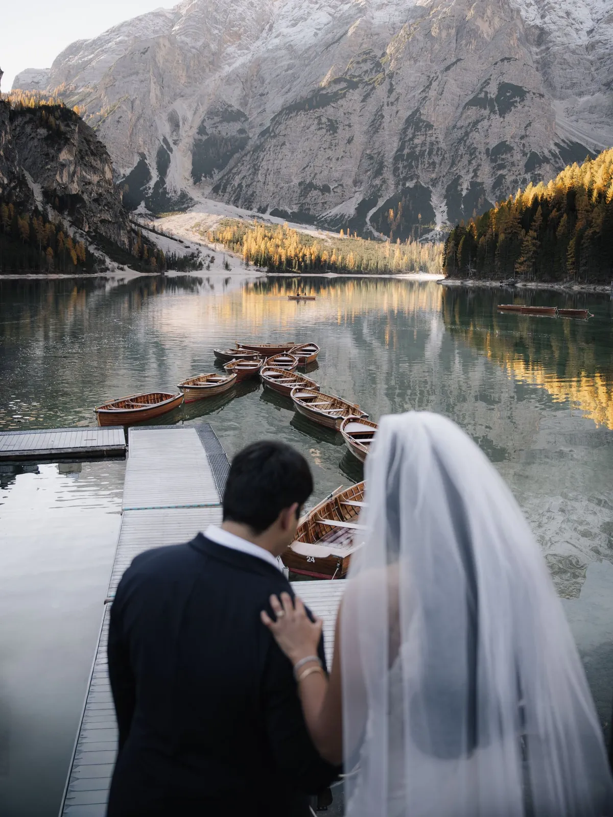Couple on the jetty overlooking the wooden boats and autumn larches of Lago di Braies